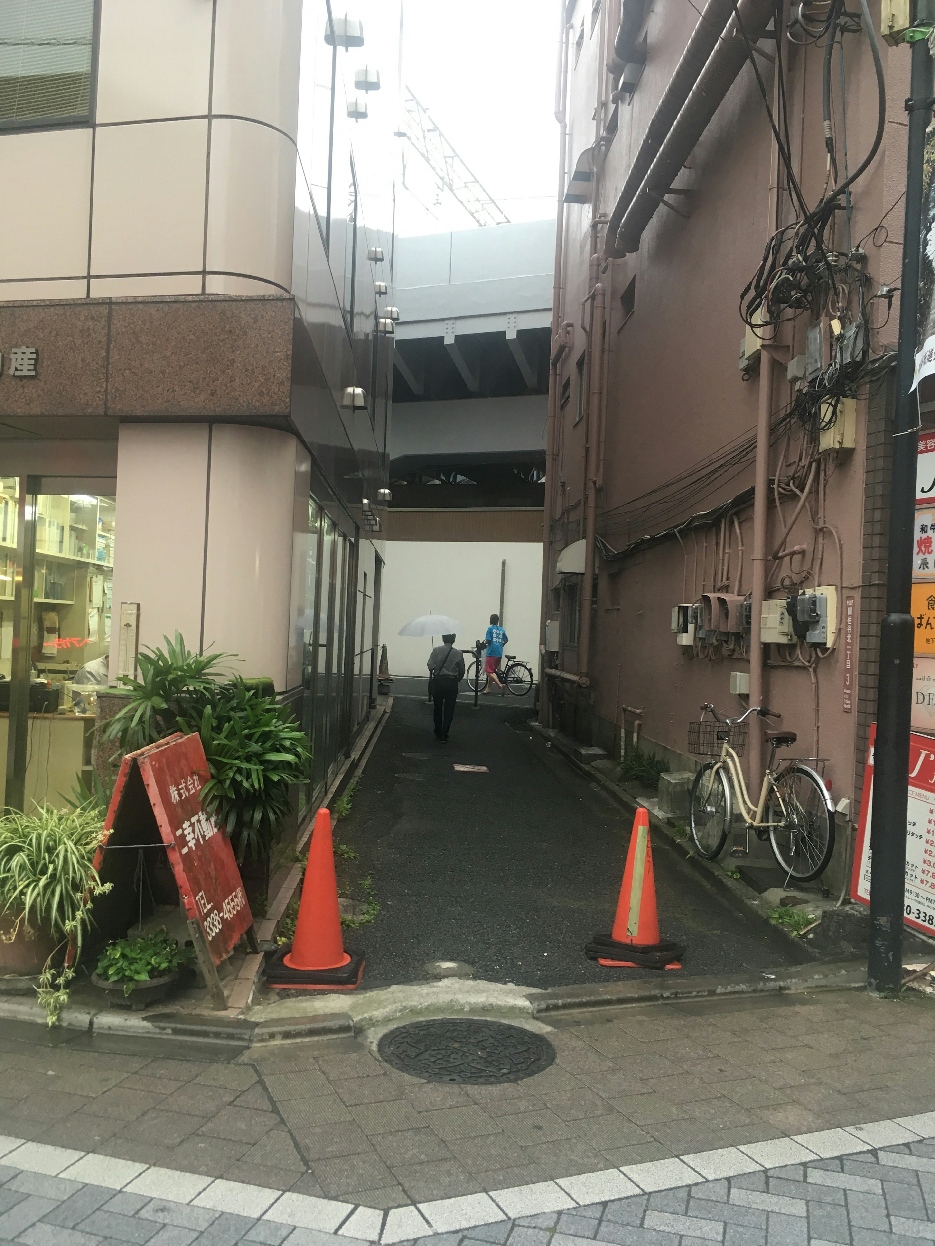 Gang sempit dengan kerucut oranye dan seseorang berjalan di latar belakang