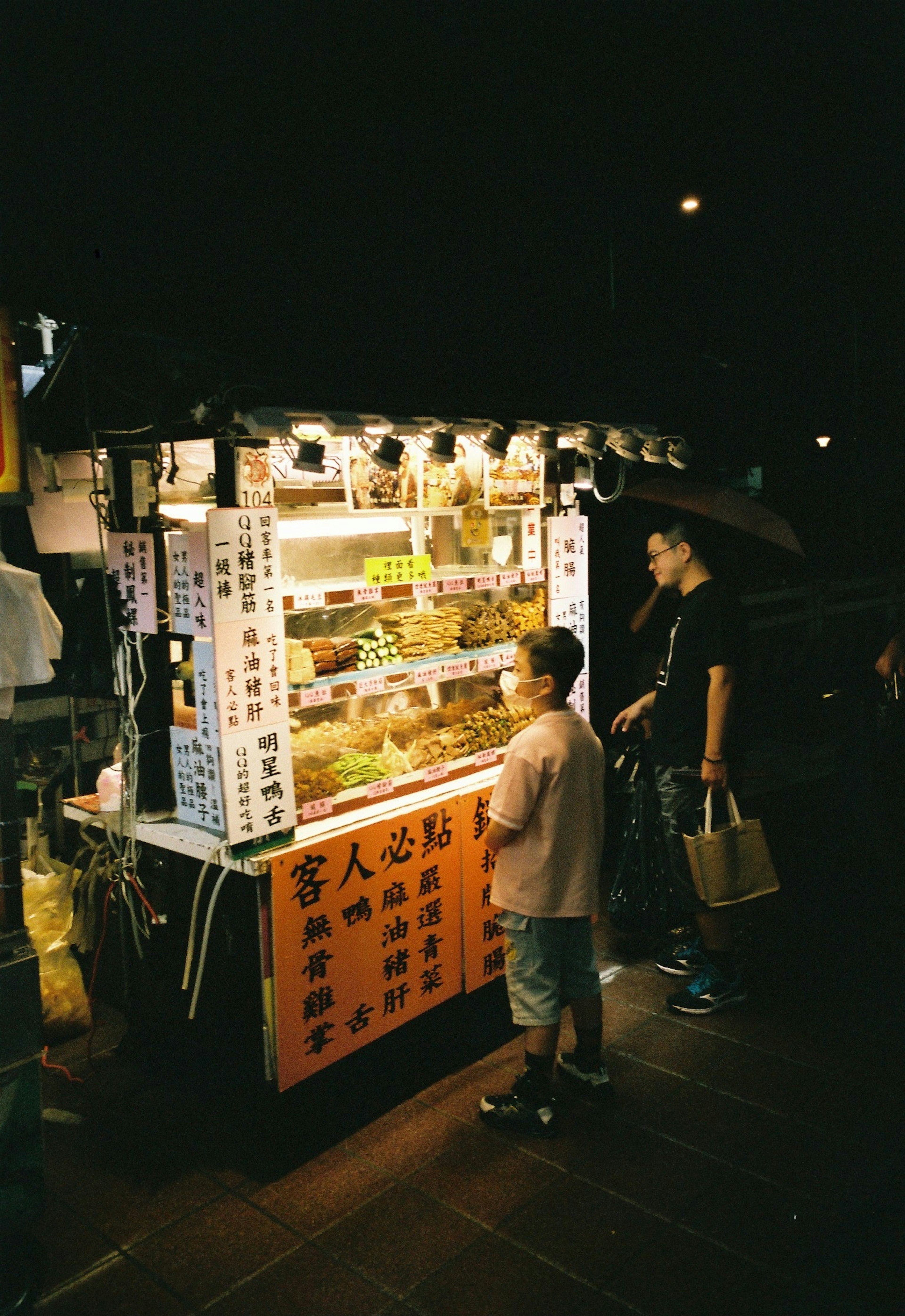 夜の屋台で食べ物を選ぶ子供と大人の姿