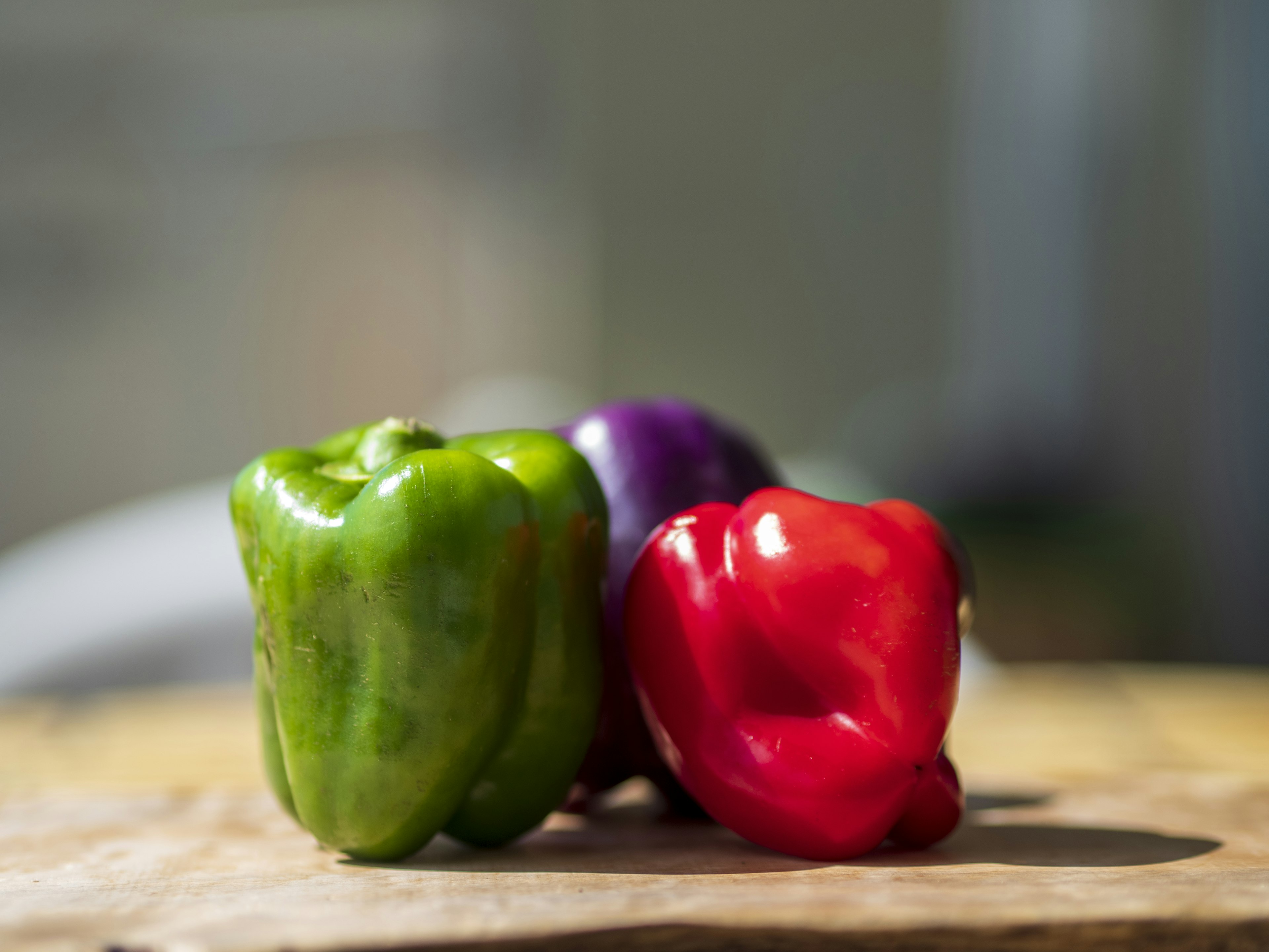 Green red and purple bell peppers arranged on a wooden board