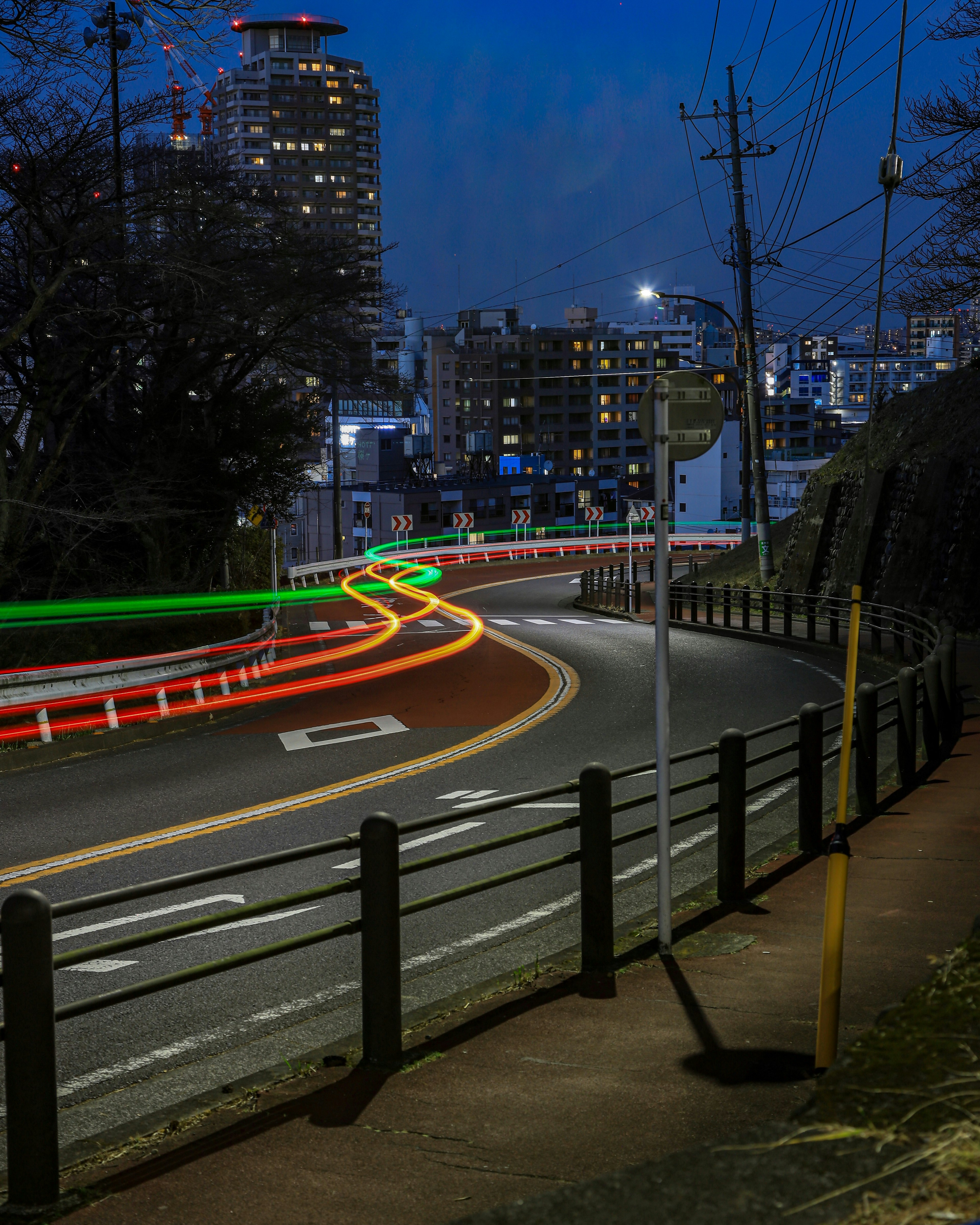 Kurvige Straße mit Lichtspuren von Fahrzeugen vor einer nächtlichen Stadtlandschaft