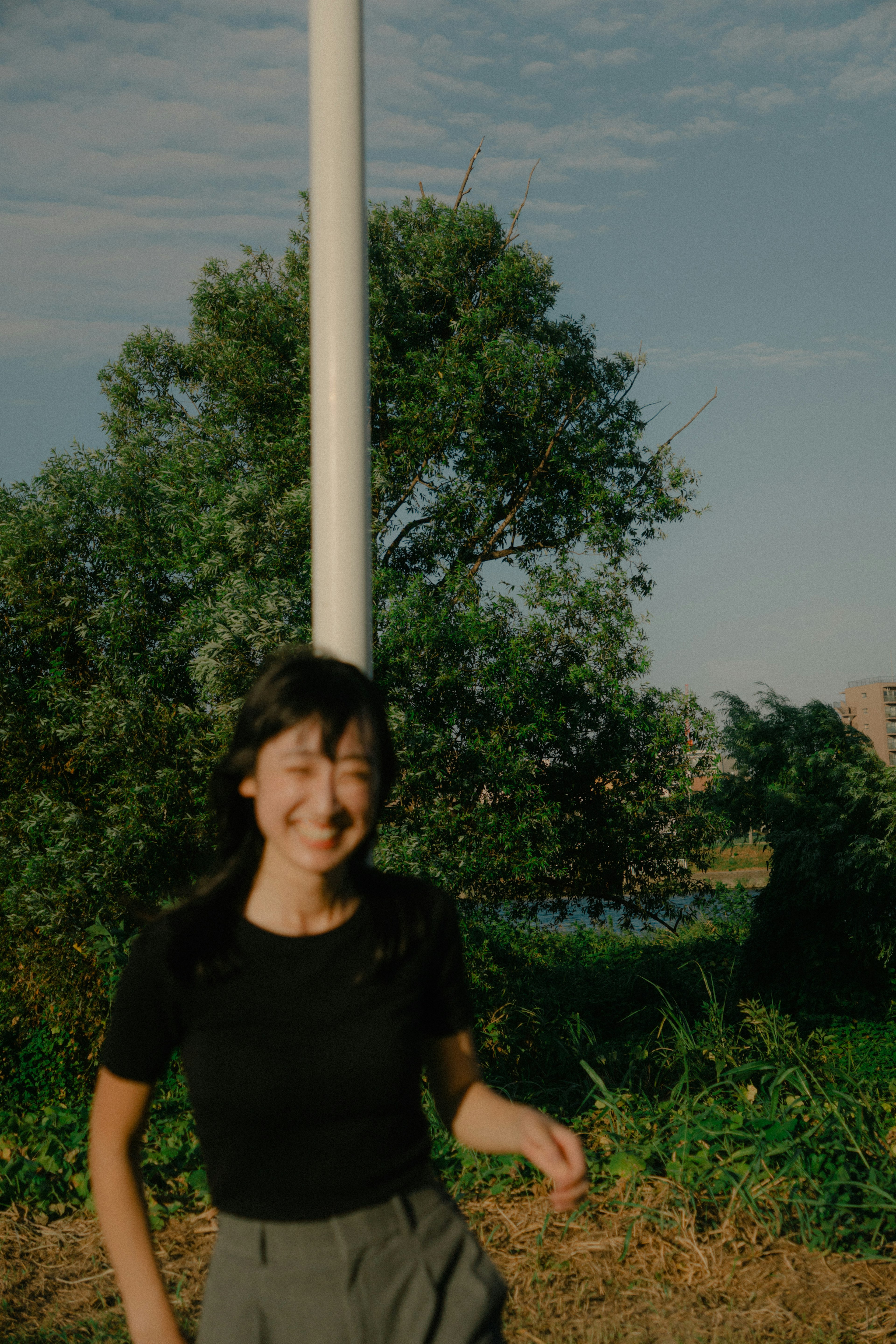 A woman smiling while running in a green outdoor setting with trees and a blue sky