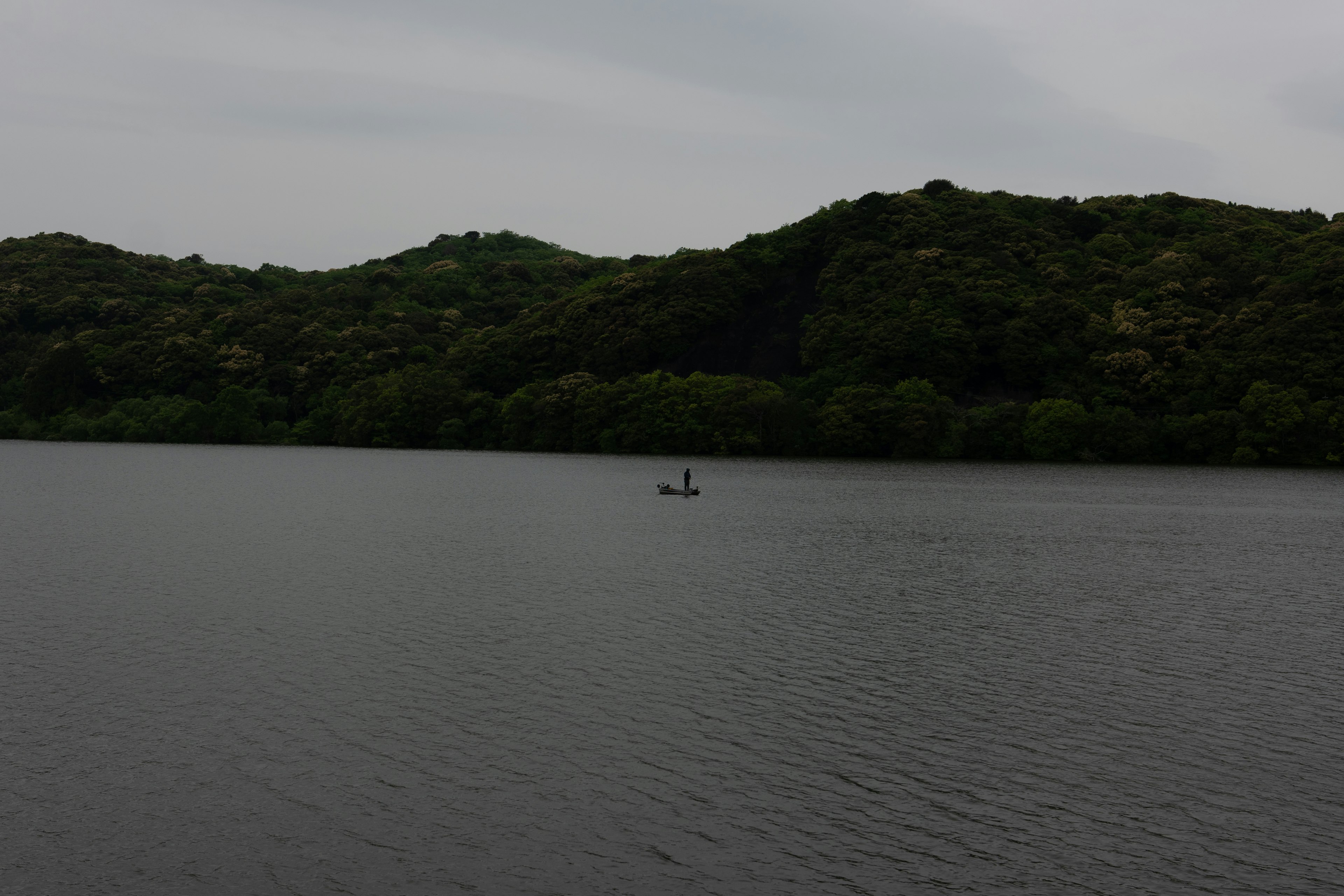 Dos personas en un bote en un lago tranquilo rodeado de colinas verdes