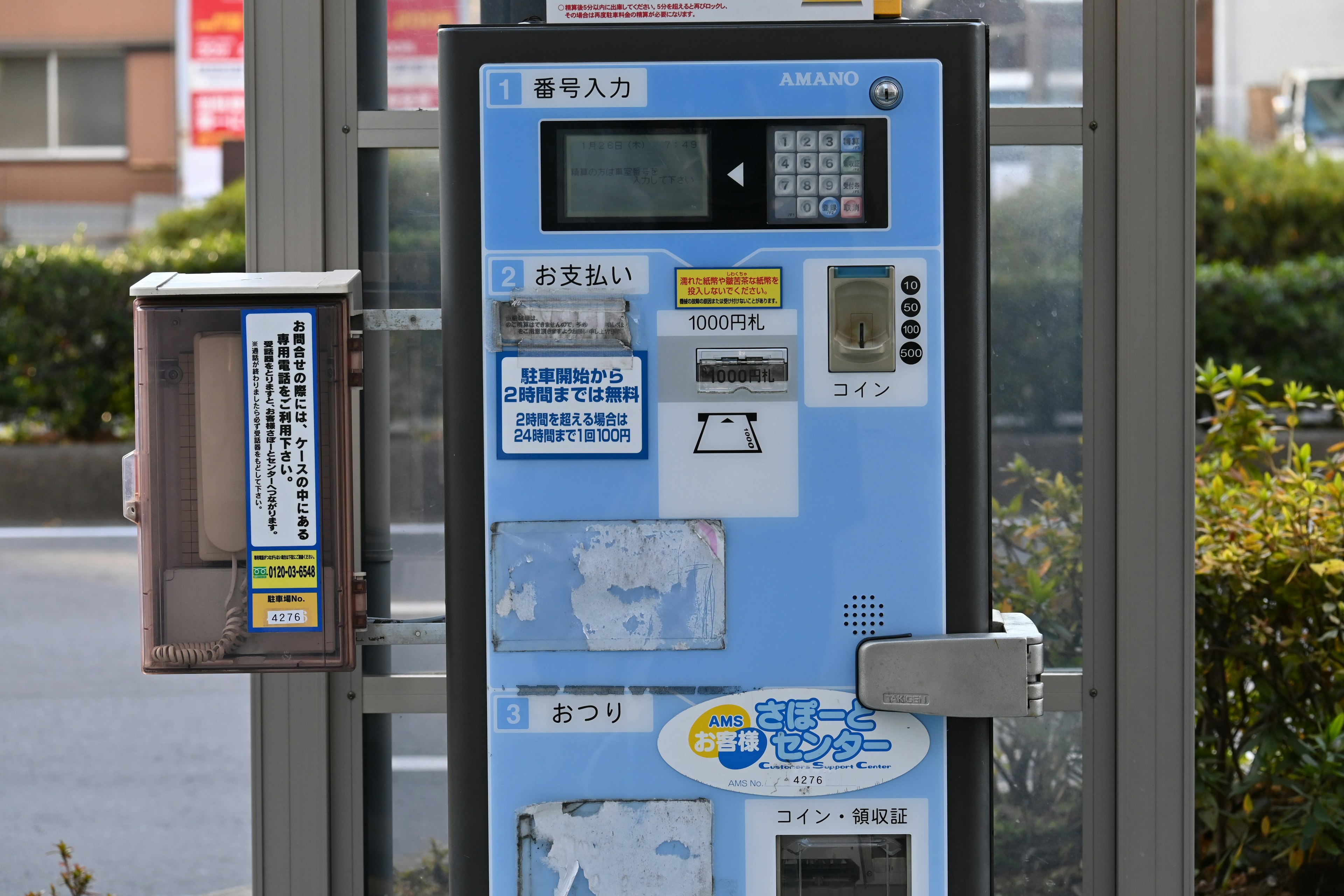 青い自動販売機が近くに立っている風景で周囲には緑の植え込みがある