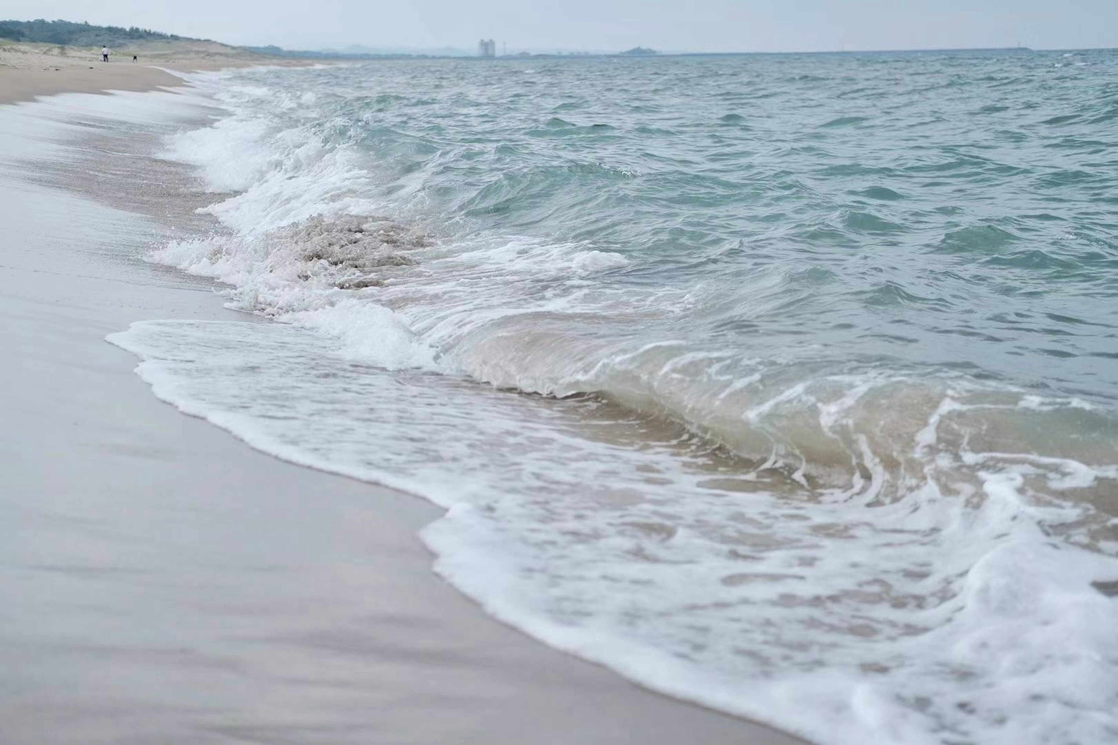 Onde gentili che si infrangono su una spiaggia sabbiosa sotto un cielo nuvoloso