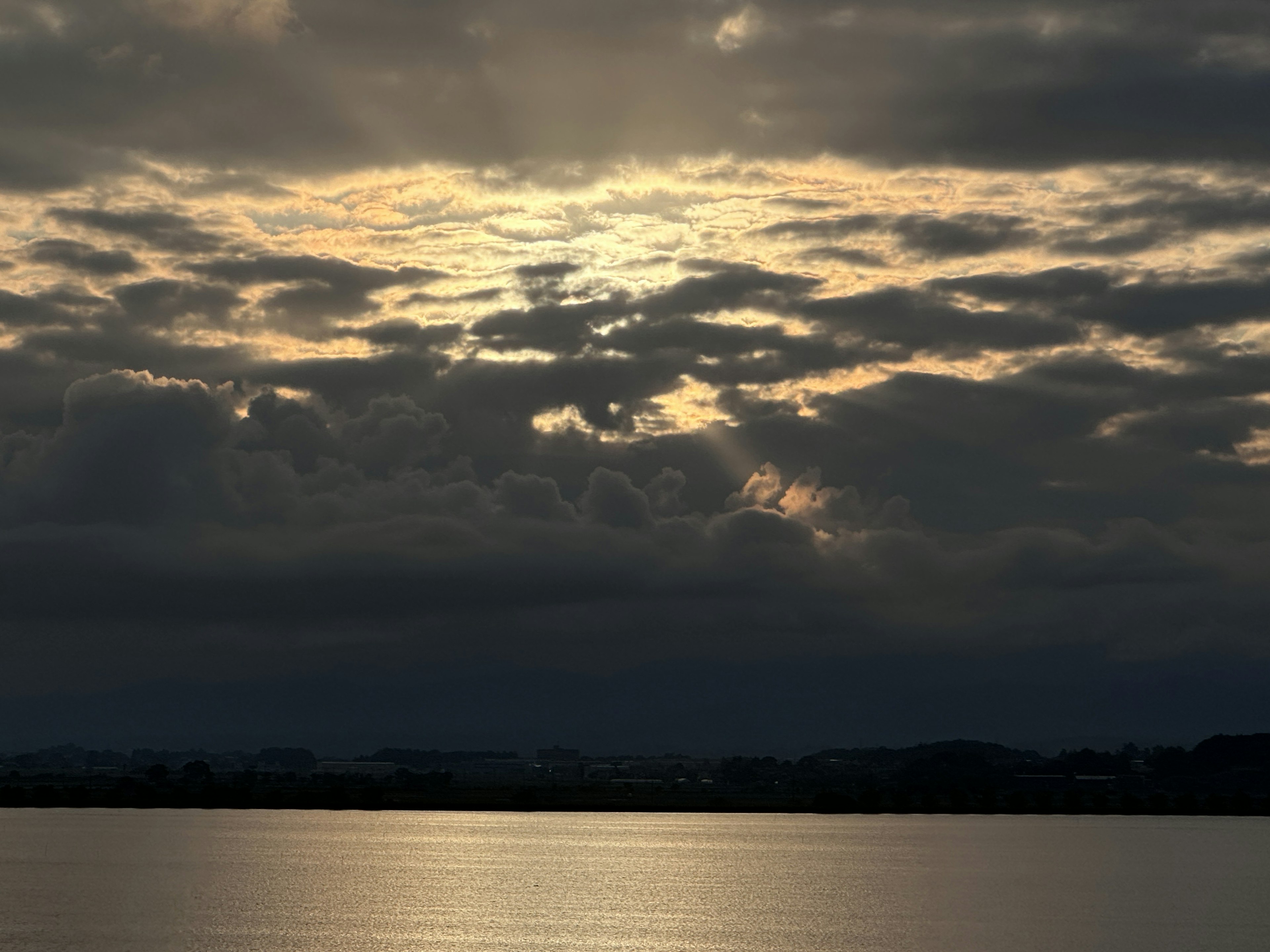 A landscape with sunlight breaking through cloudy skies illuminating the water surface