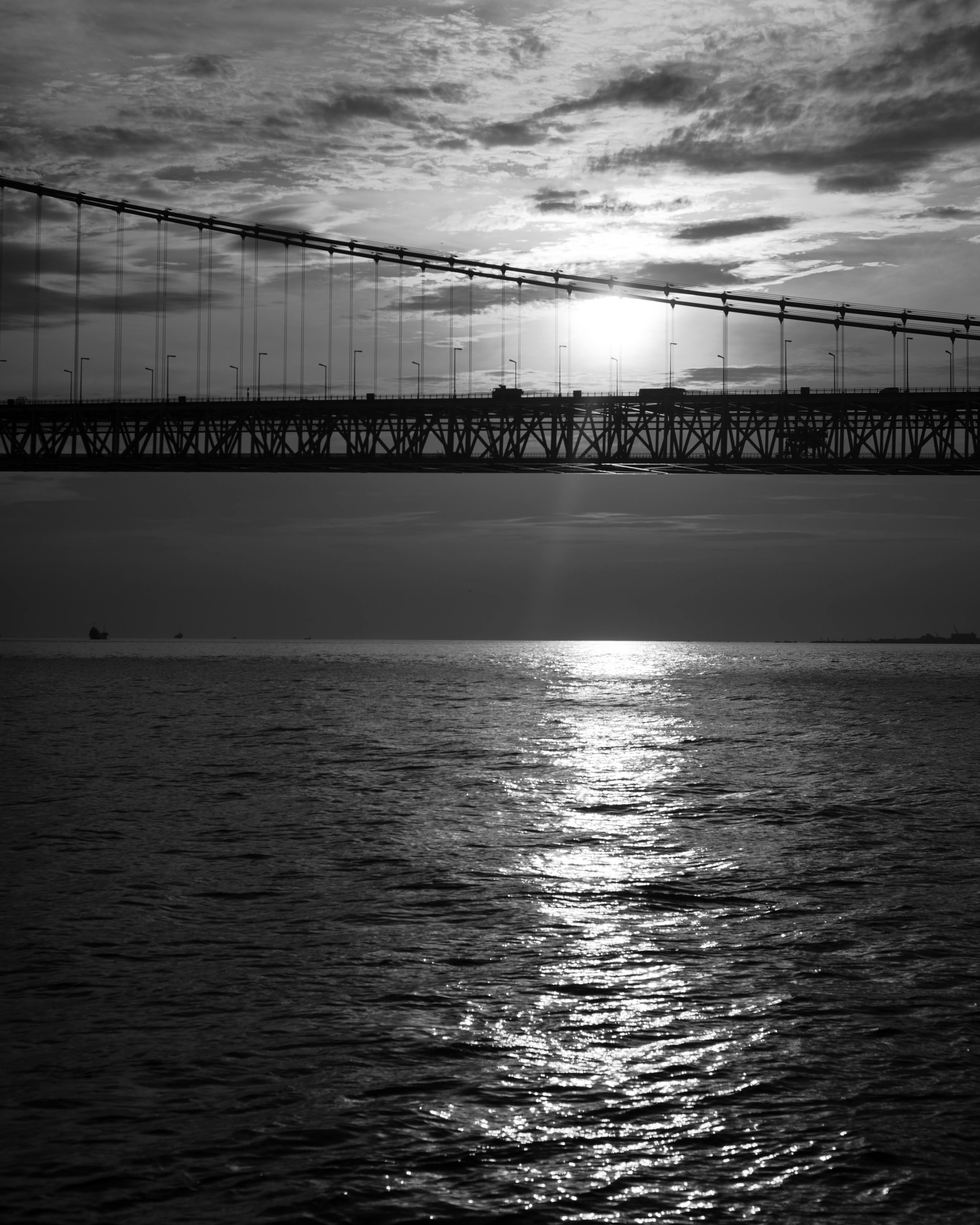 Schwarz-weiß Landschaft mit einer Brücke und Sonnenuntergangsreflexion auf dem Wasser