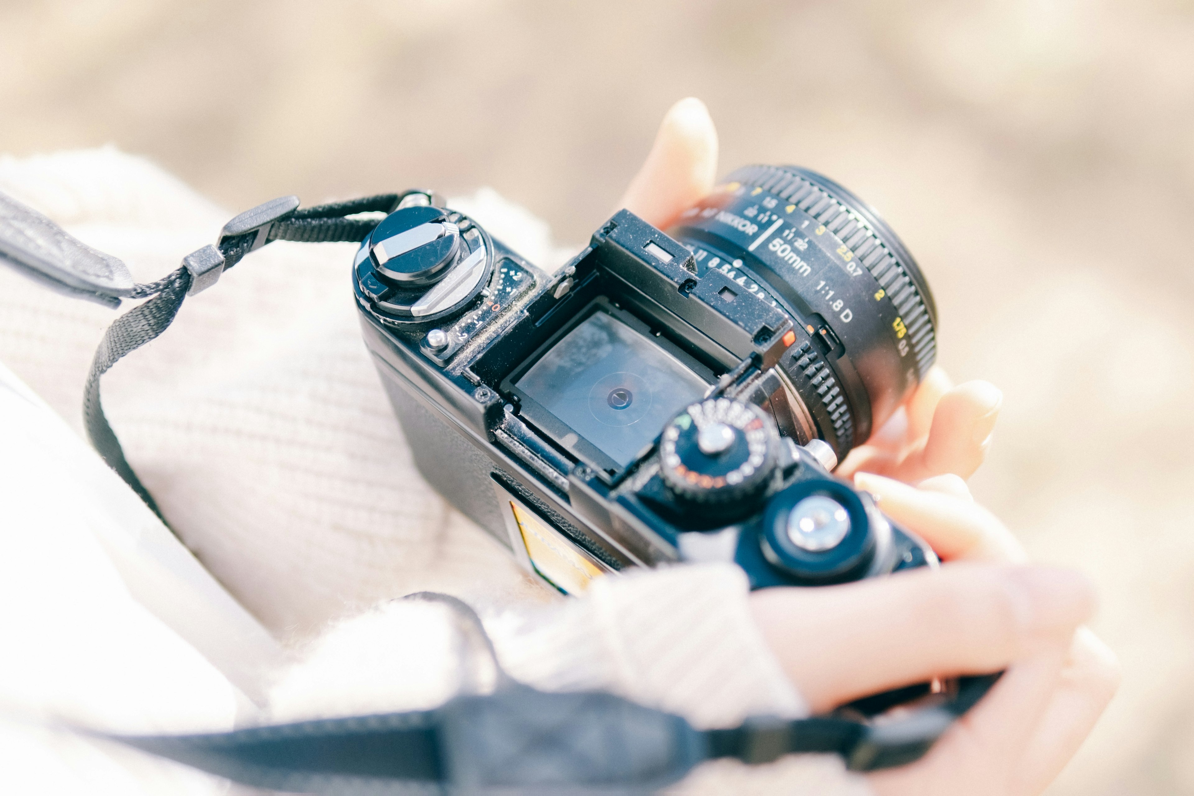 Close-up of hands holding a camera with a bright lens and blurred background