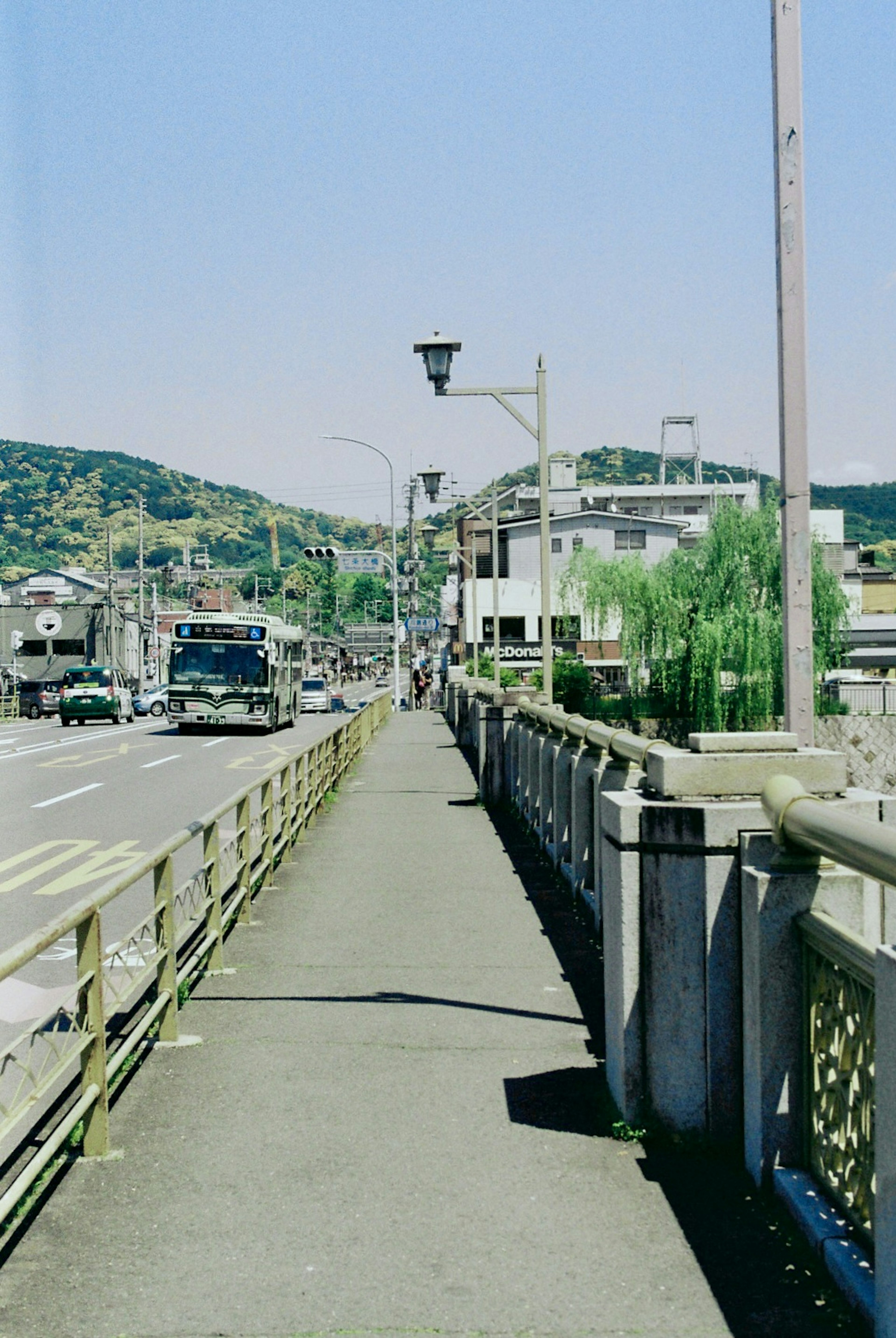 Scenic view of a walkway beside a road with green hills in the background and streetlights