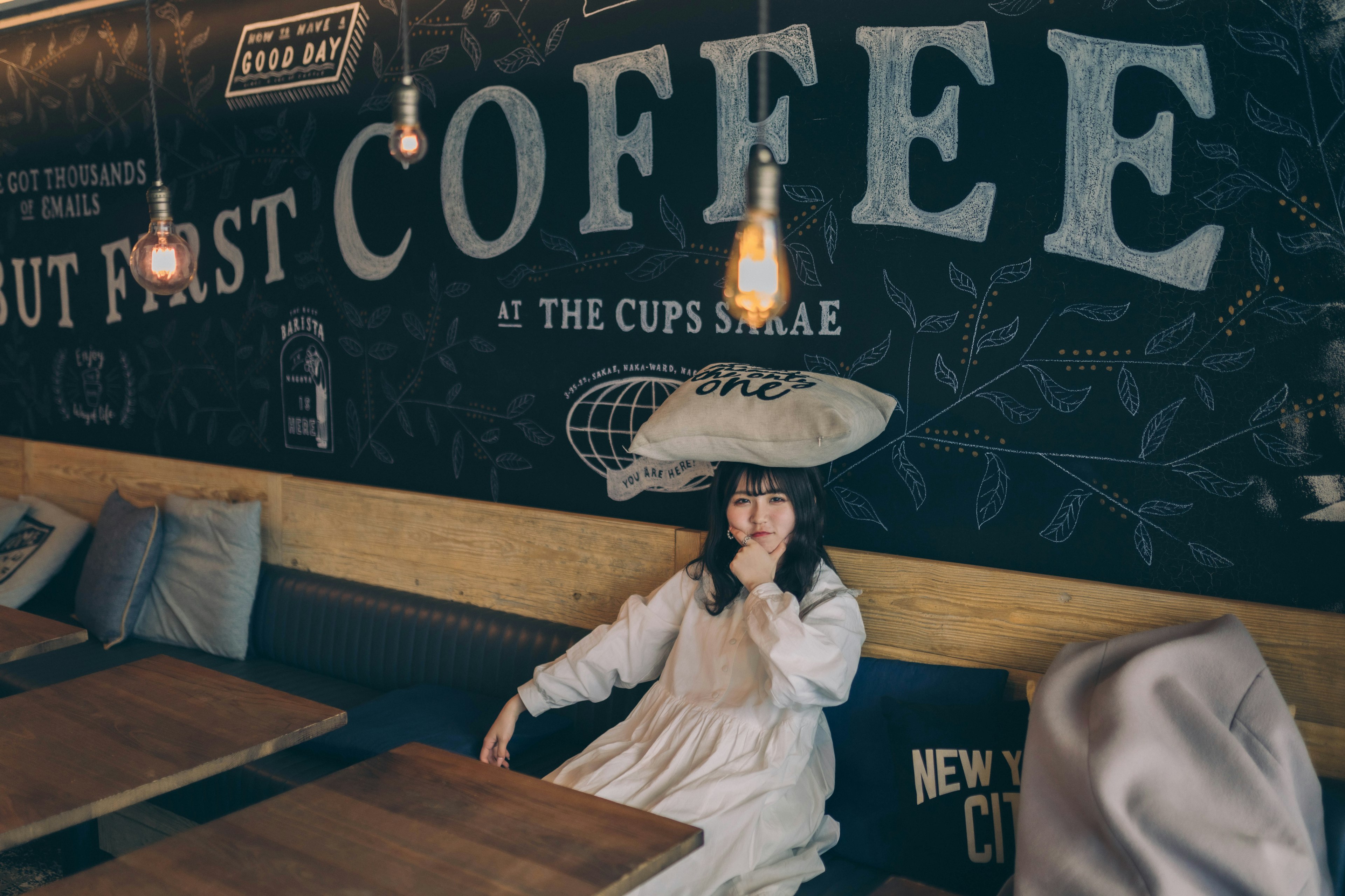 Mujer sentada en un café con una almohada en la cabeza bebiendo café