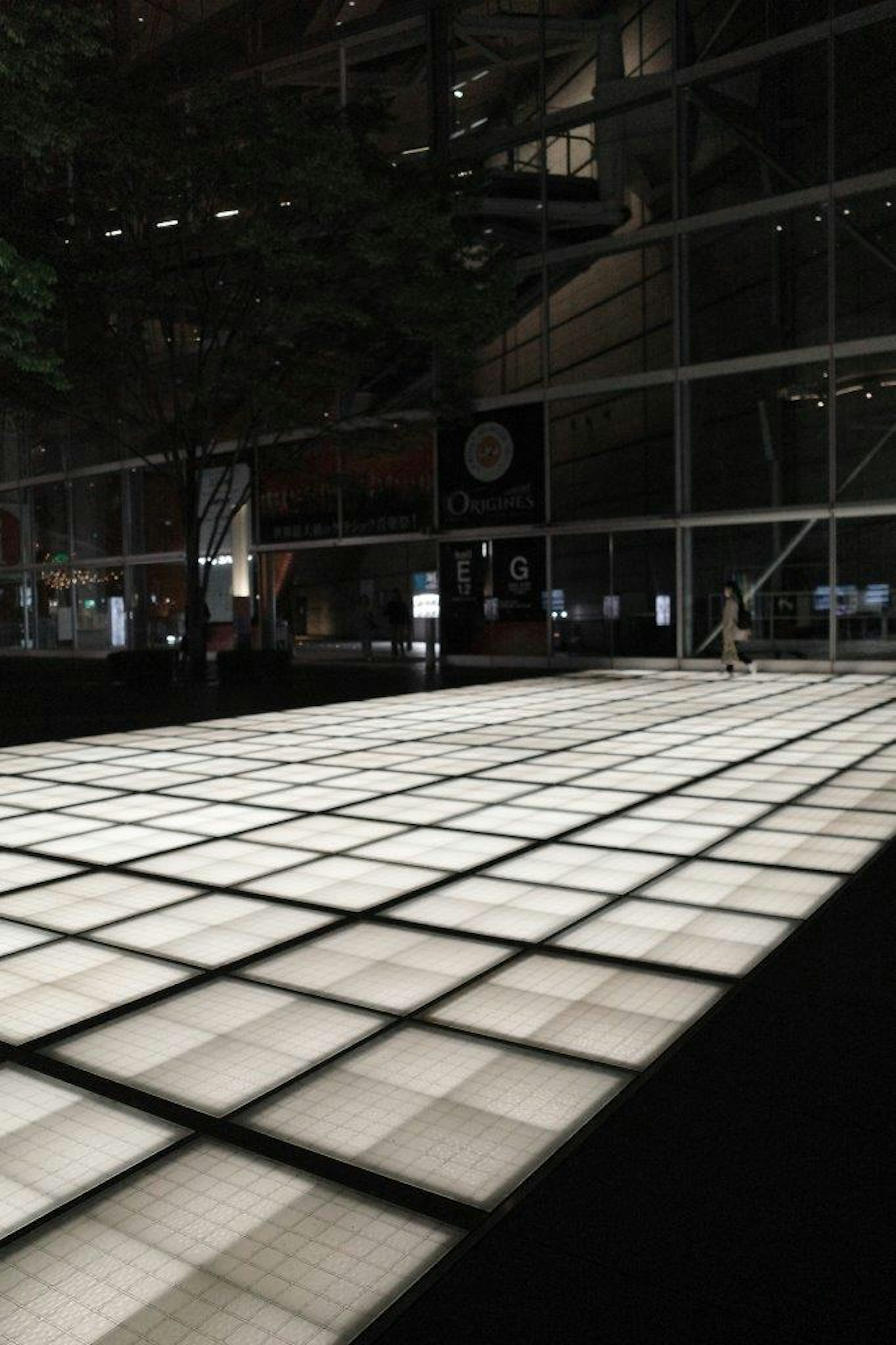 Illuminated white tiled floor in a dark environment with surrounding building windows