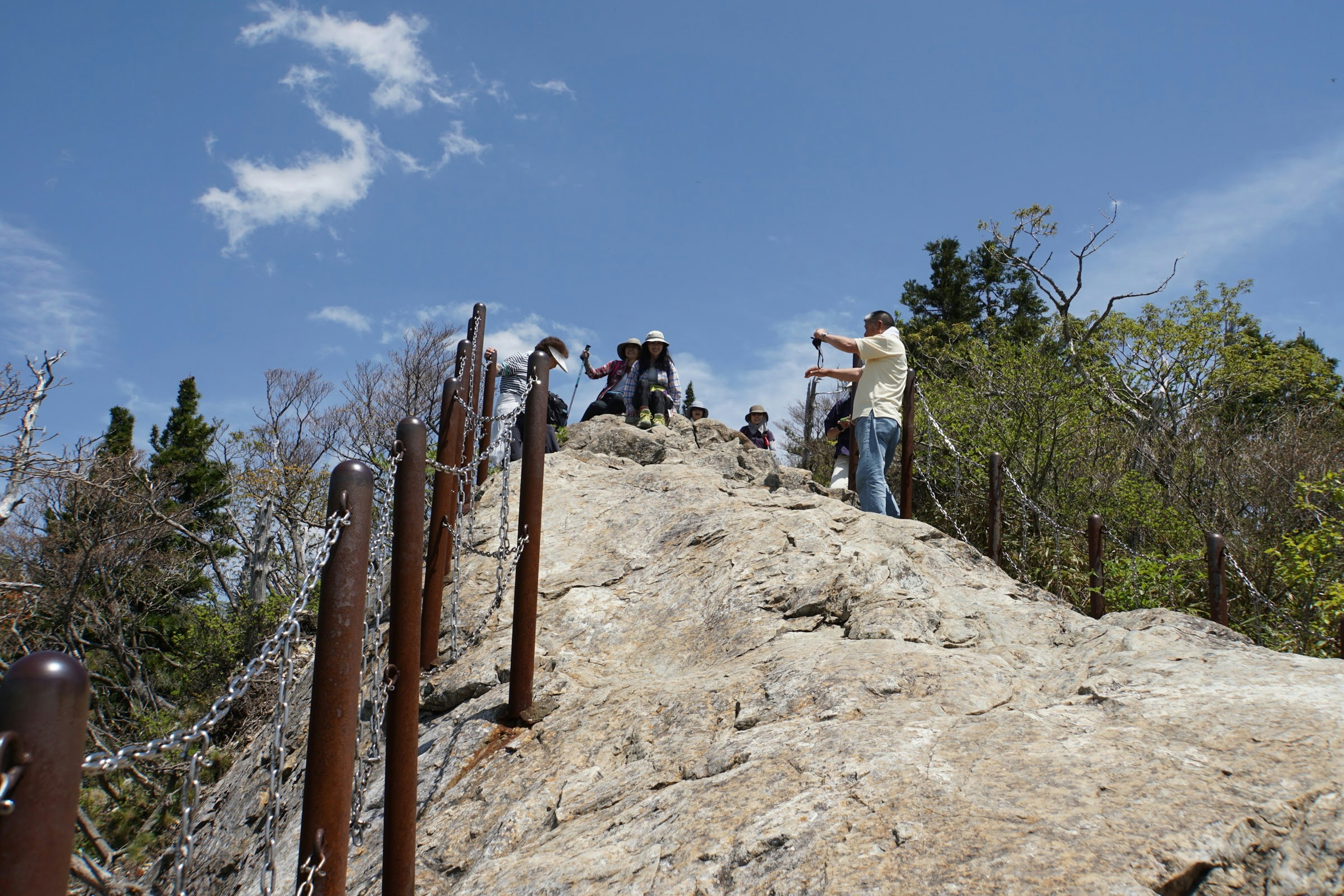 Personas en un sendero rocoso con cielo azul y vegetación de fondo