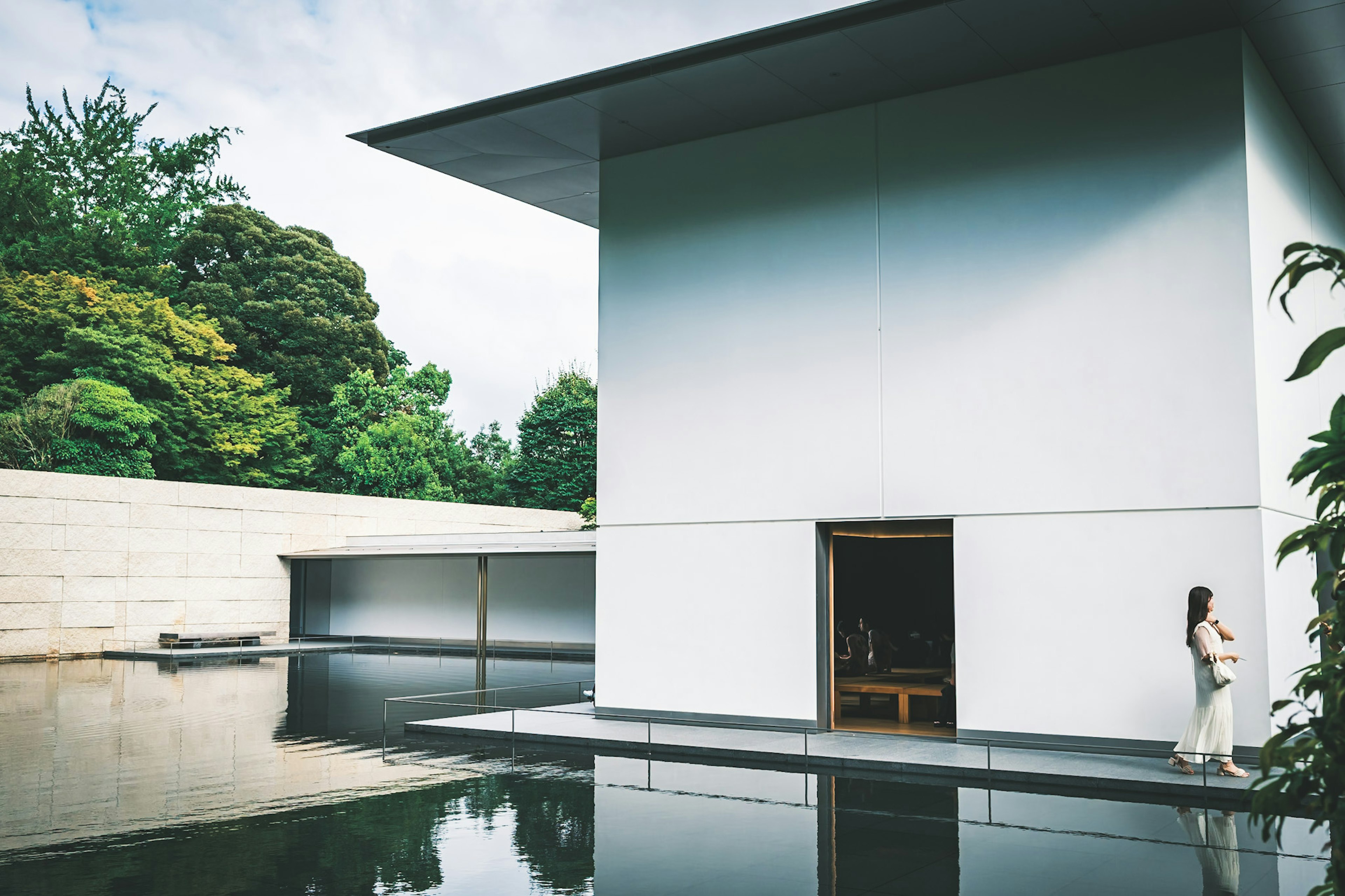 Un bâtiment moderne blanc à côté d'une surface d'eau tranquille avec une femme debout