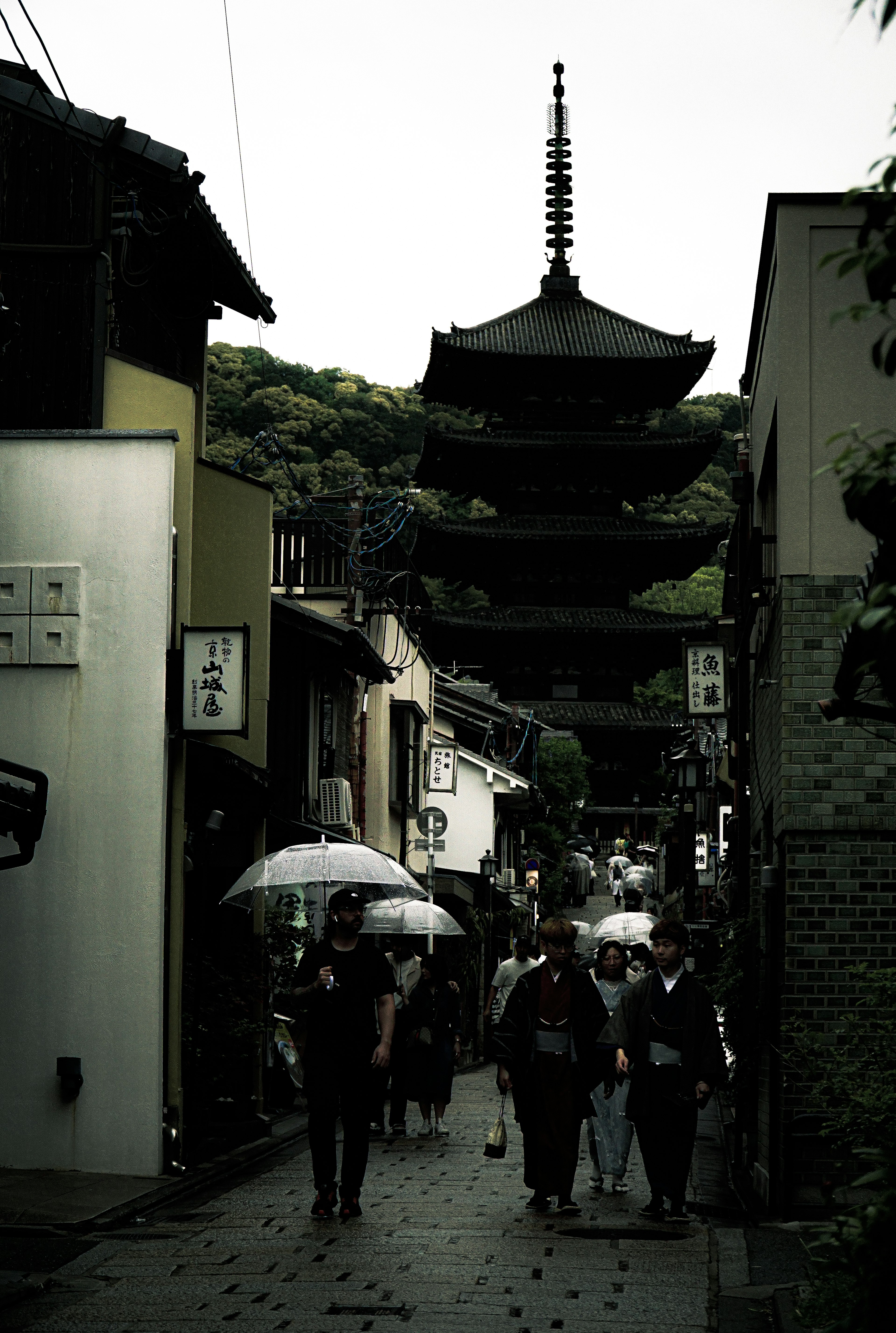 Persone che camminano sotto la pioggia con una pagoda in una strada storica