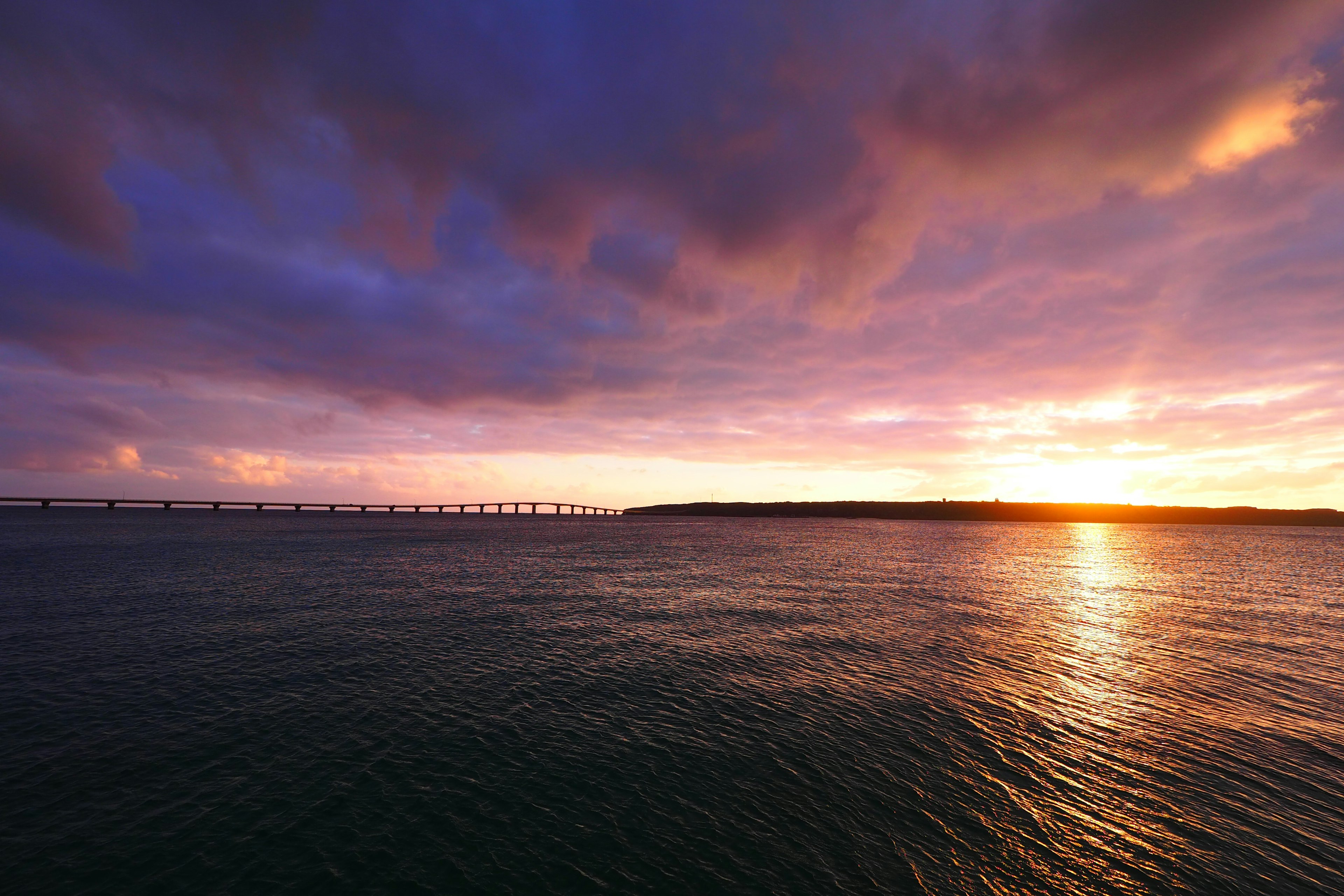 Schöner Sonnenuntergang über dem Ozean mit einer Brücke im Hintergrund