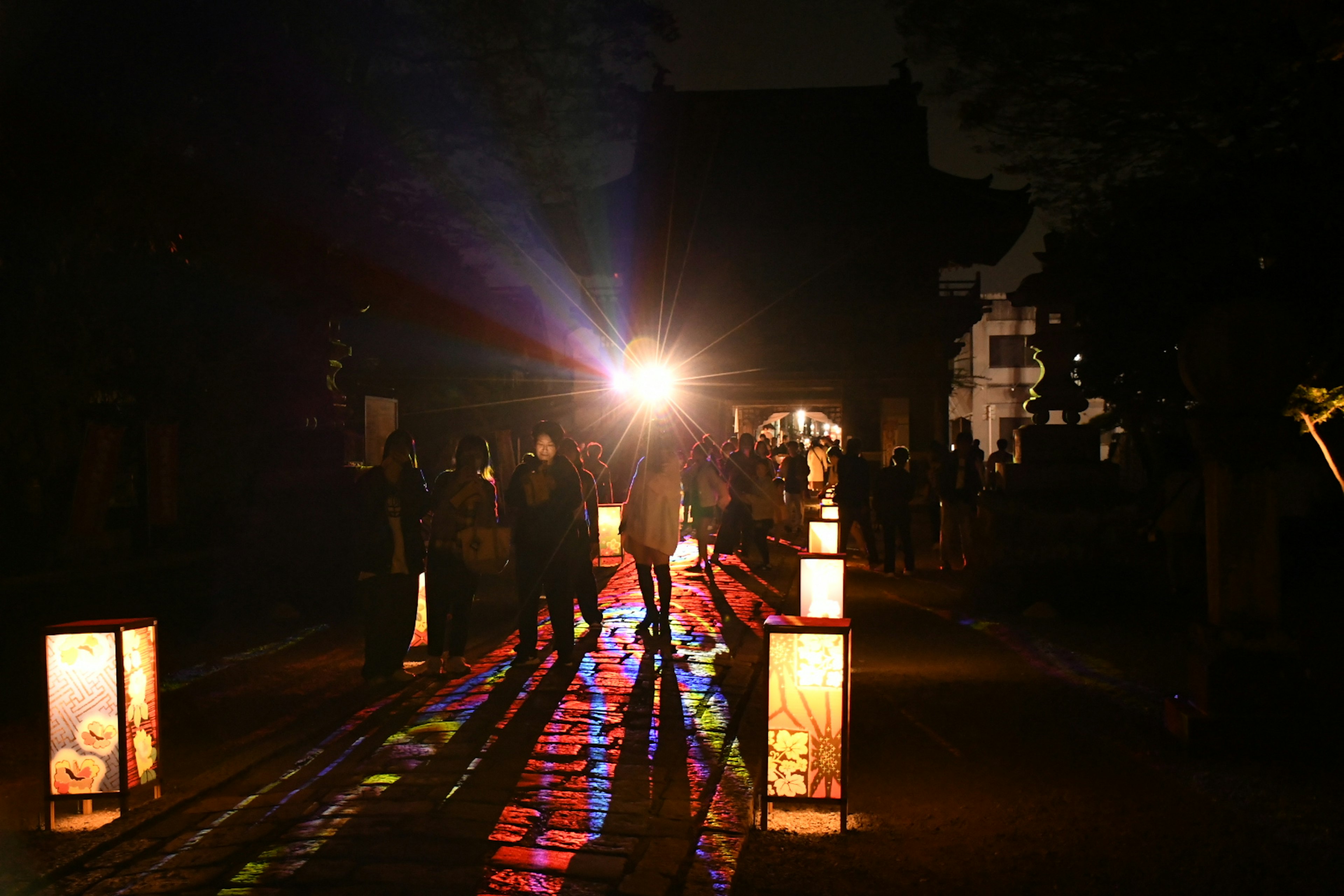 Siluetas de personas a lo largo de un camino iluminado por linternas de noche