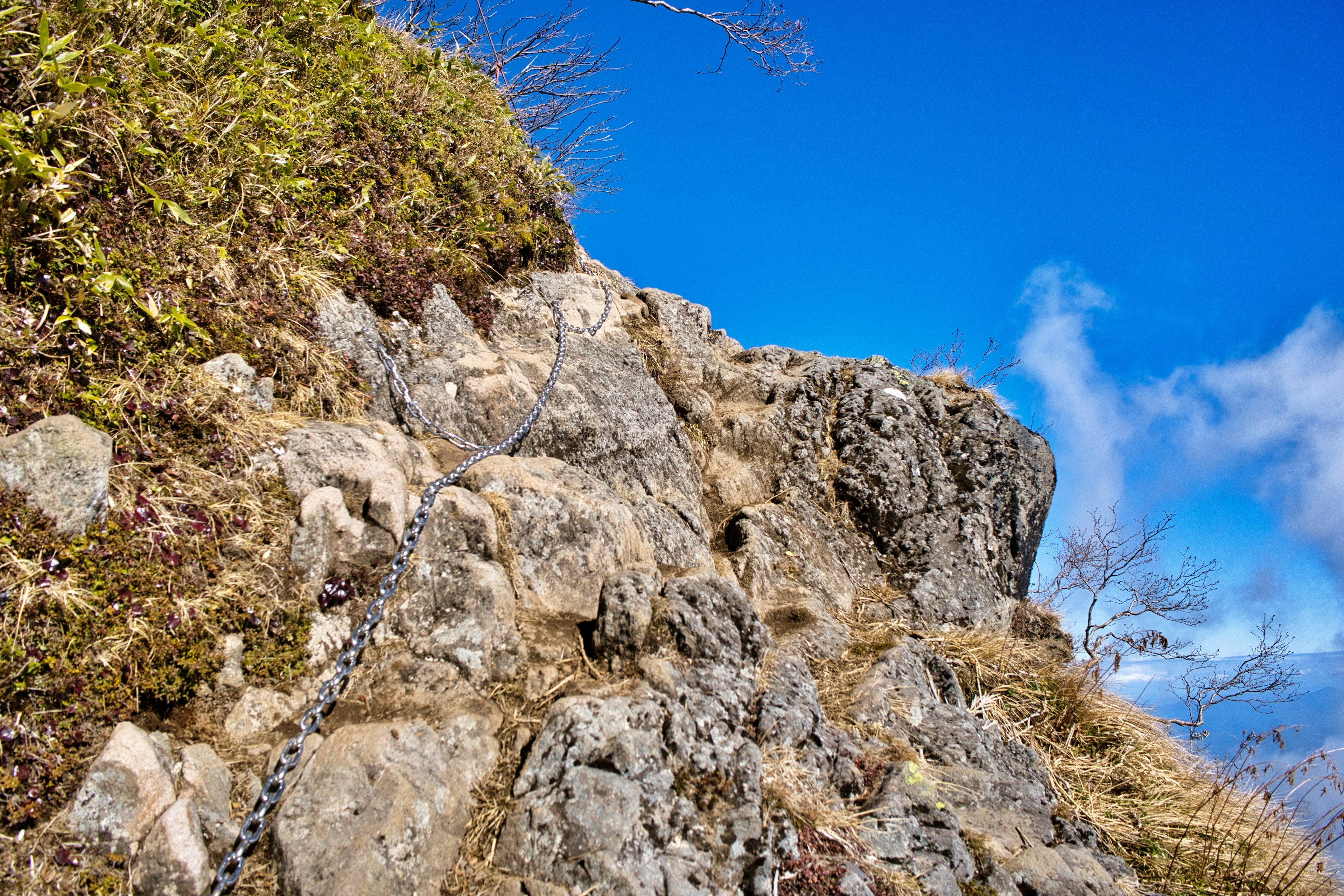 藍天和岩石地形的山地風景 鏈子連接在岩石上 綠色植物和乾草