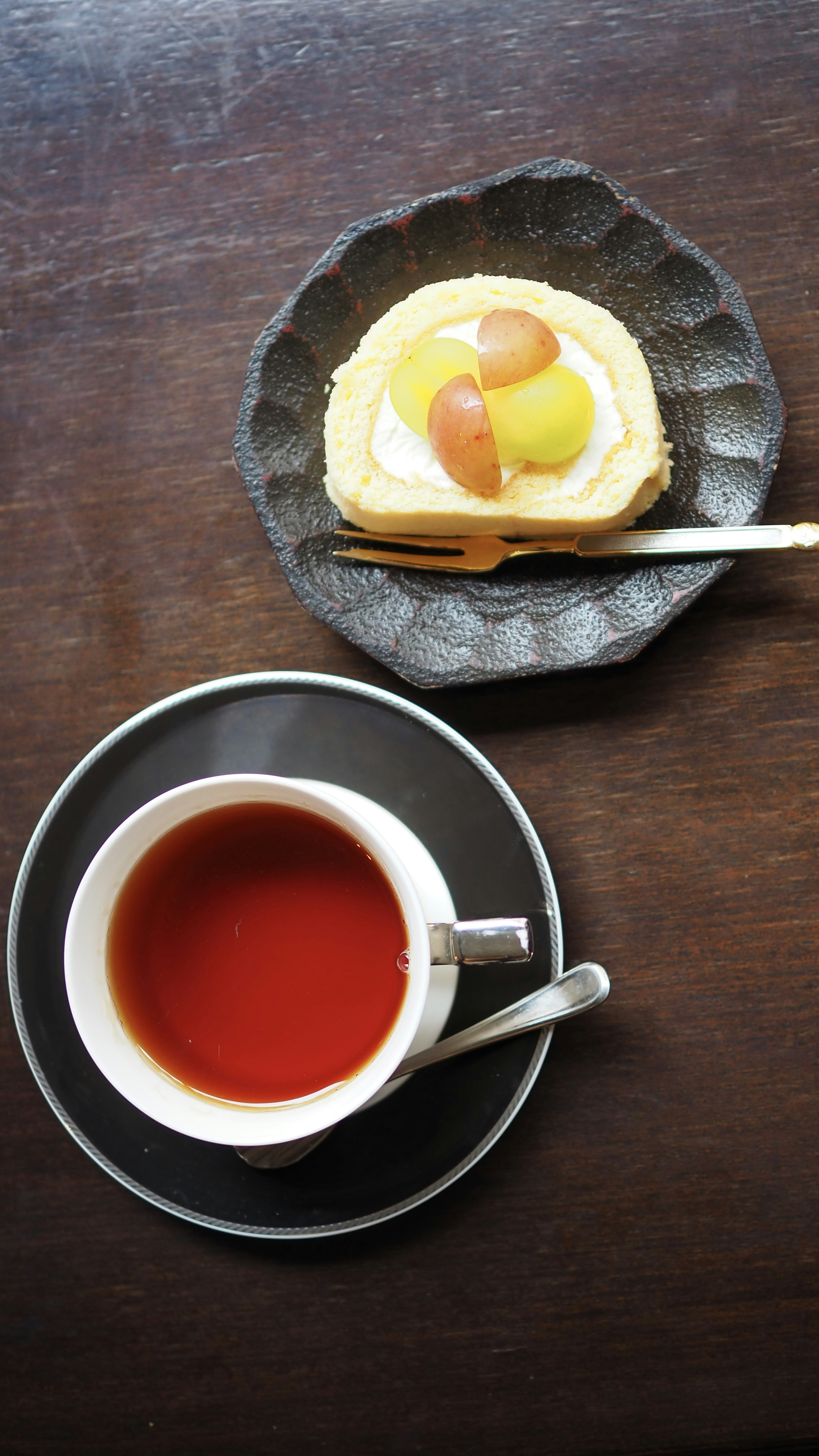 A cup of tea beside a dessert on a dark plate