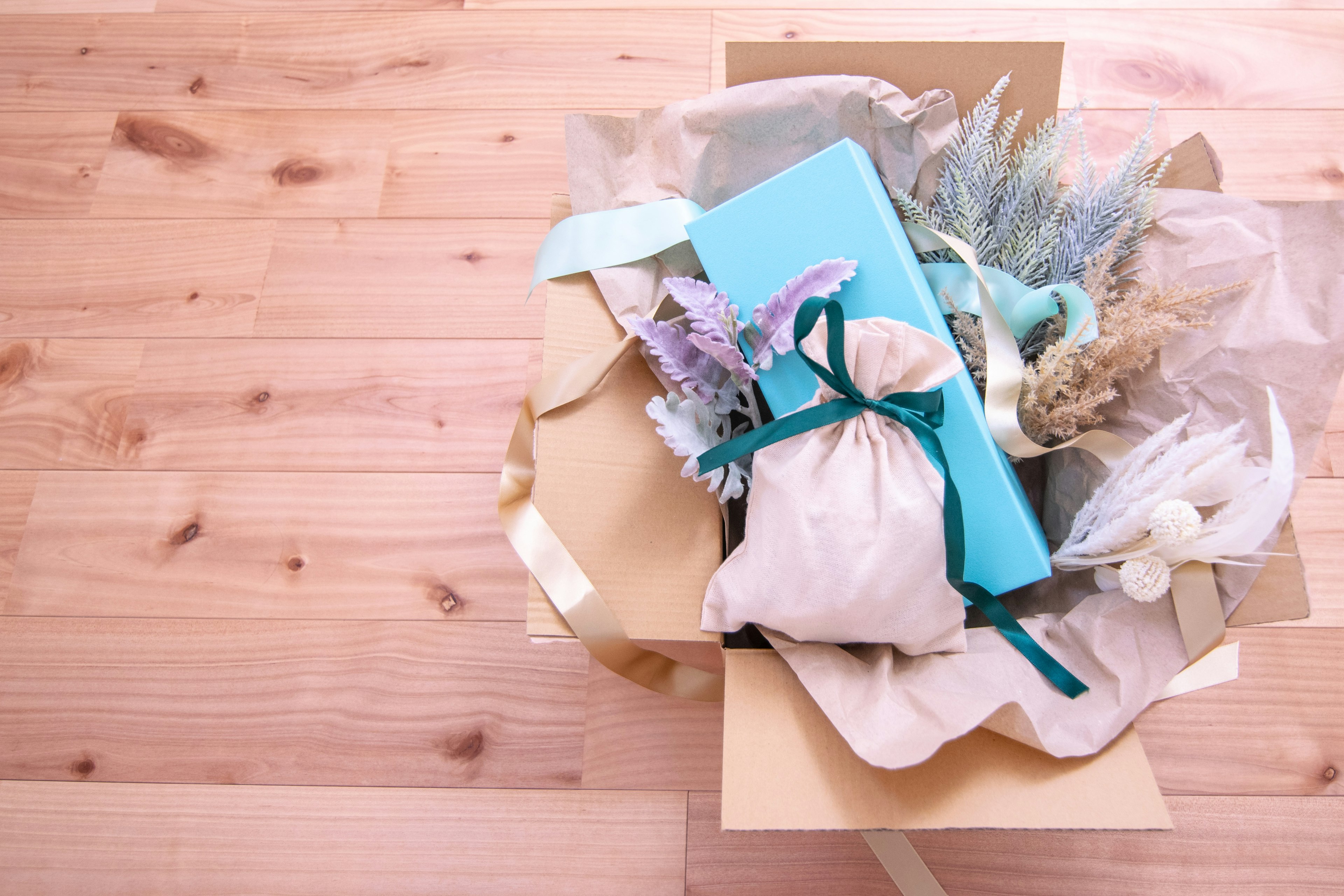 Geschenkbox mit einem blauen Geschenk und sichtbaren Trockenblumen