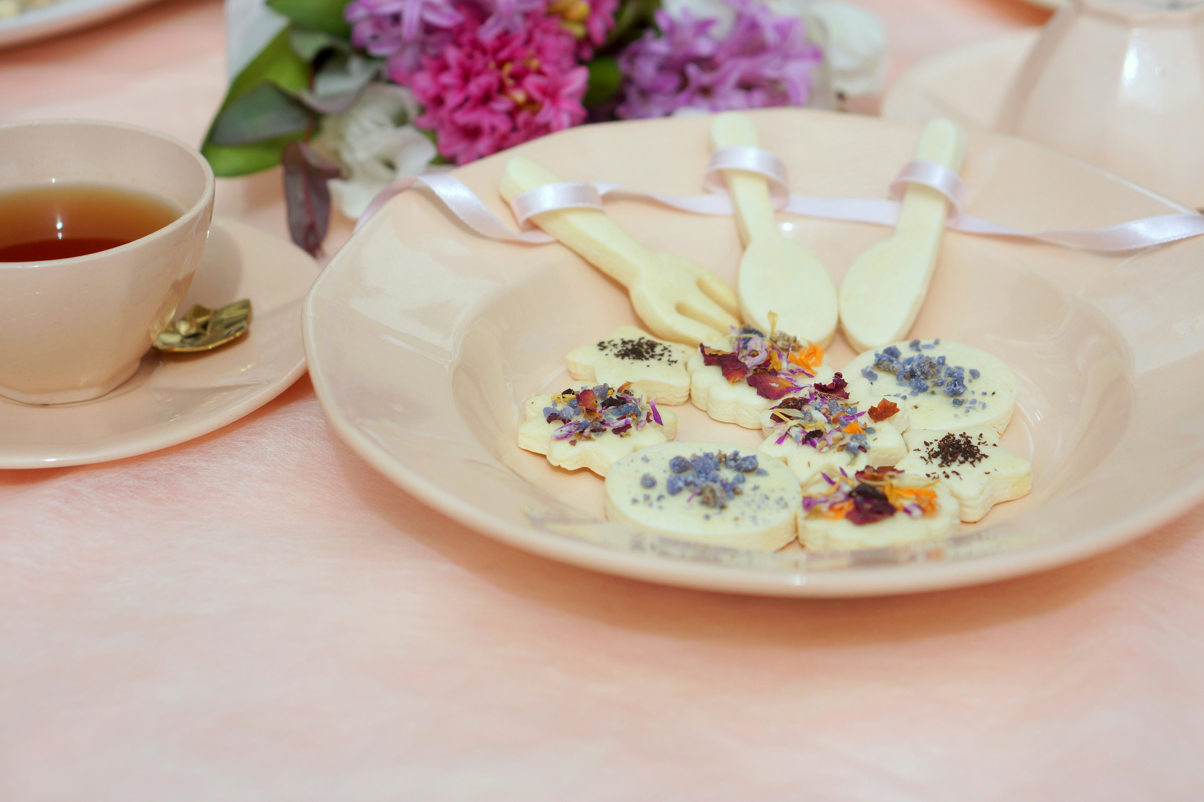 Biscotti disposti con cura con petali di fiori su un piatto accanto a una tazza di tè