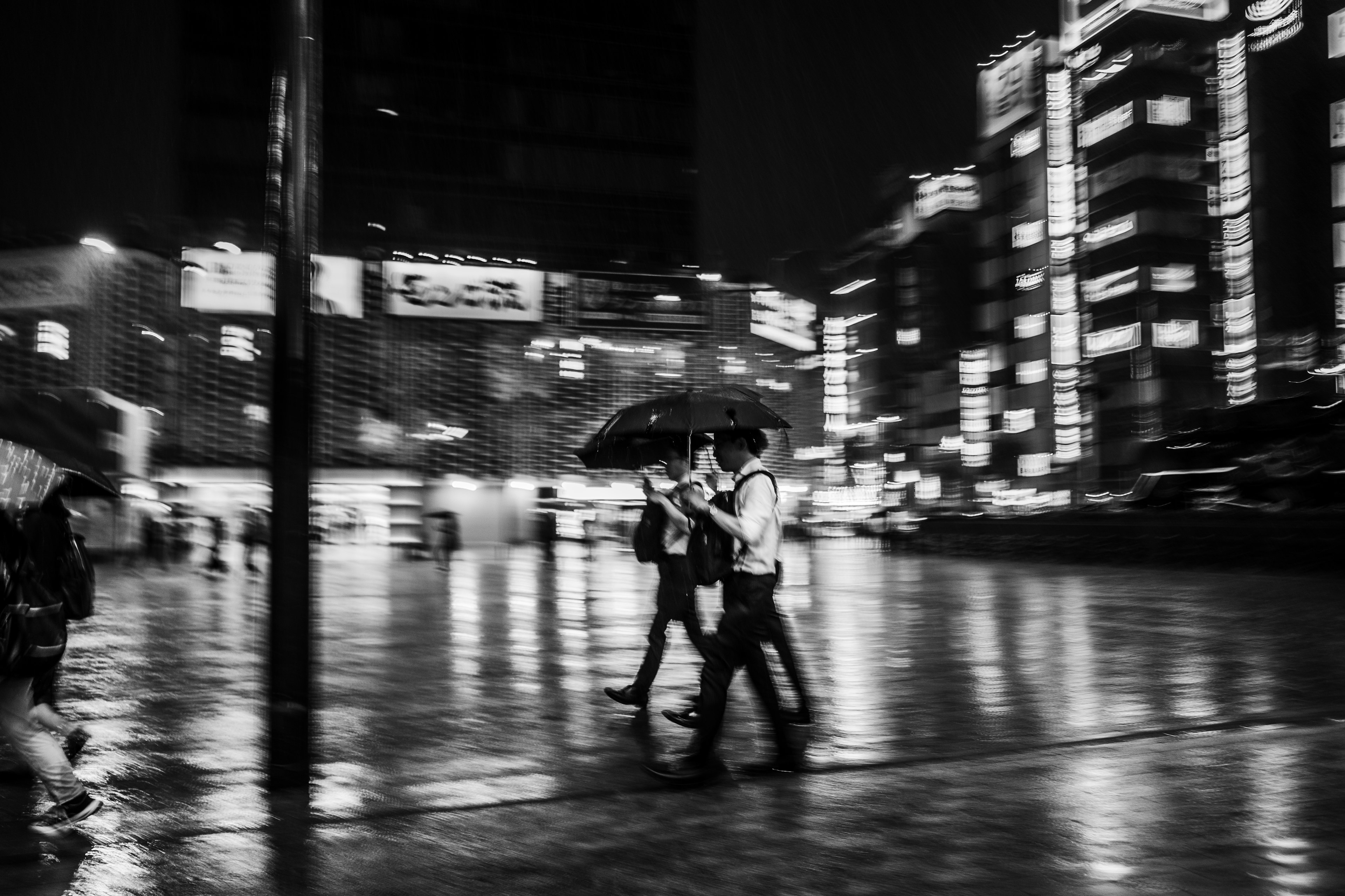 Una foto in bianco e nero di una coppia che cammina con ombrelli in città di notte