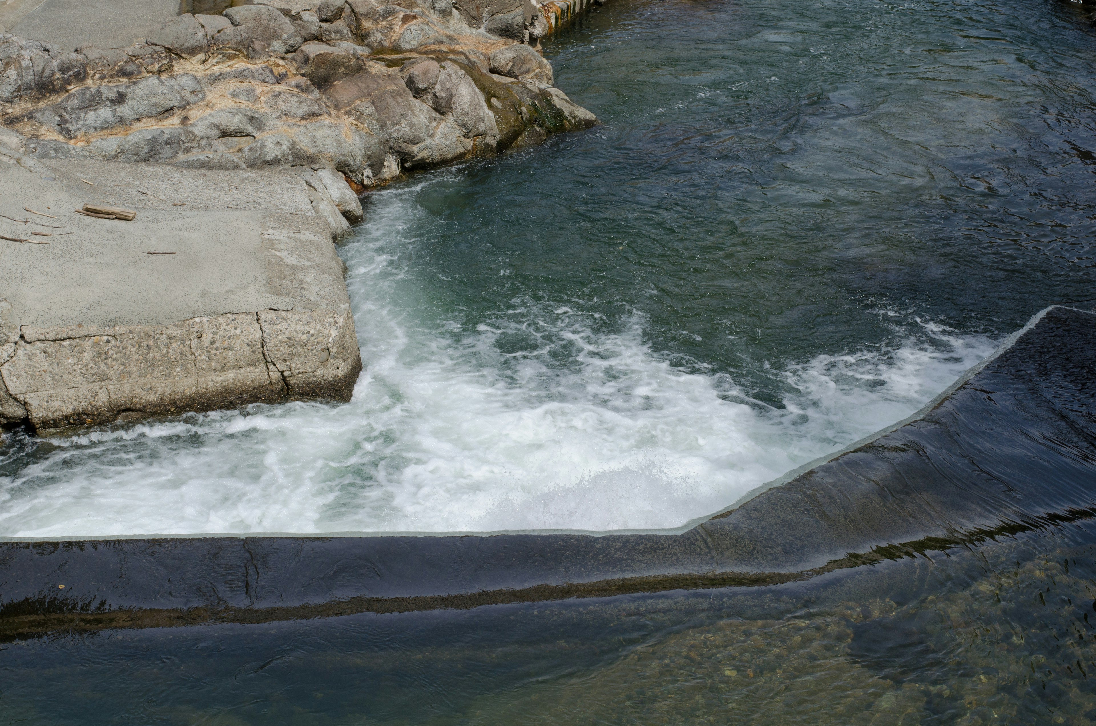 Flowing water over rocks with a concrete edge