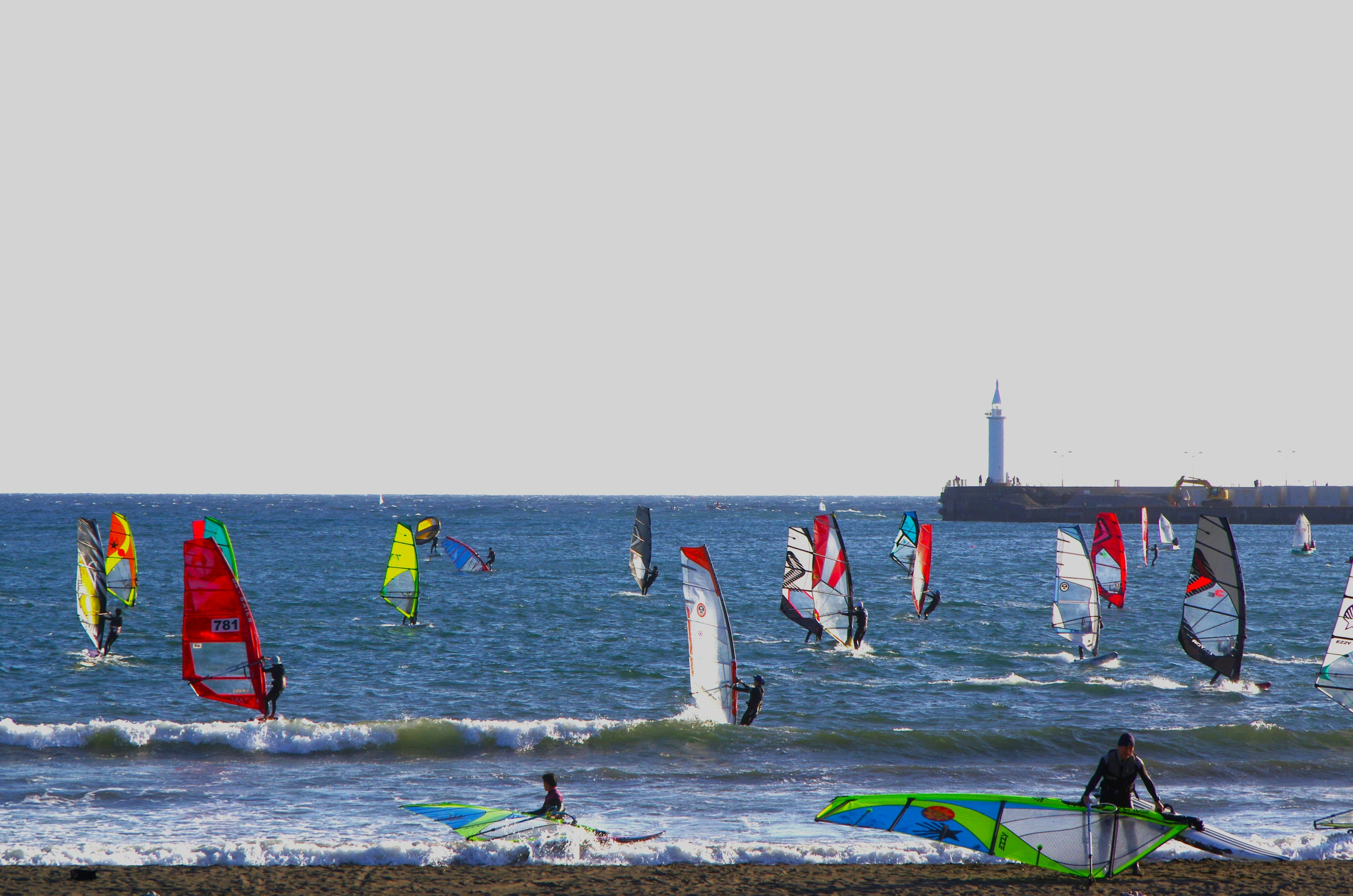 Personas disfrutando del windsurf en el mar con un faro al fondo