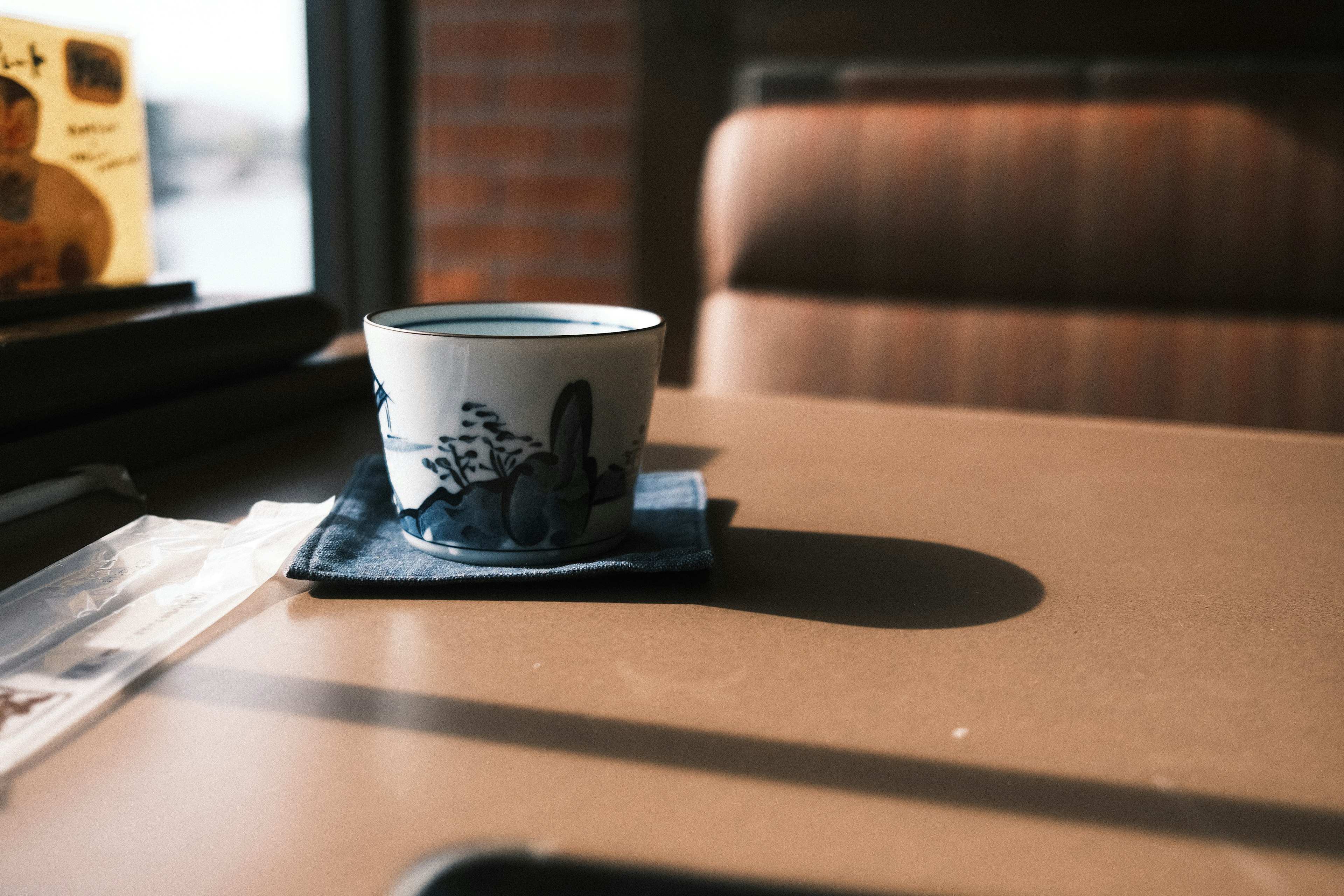 A blue patterned teacup on a table with a saucer sunlight streaming in from the window