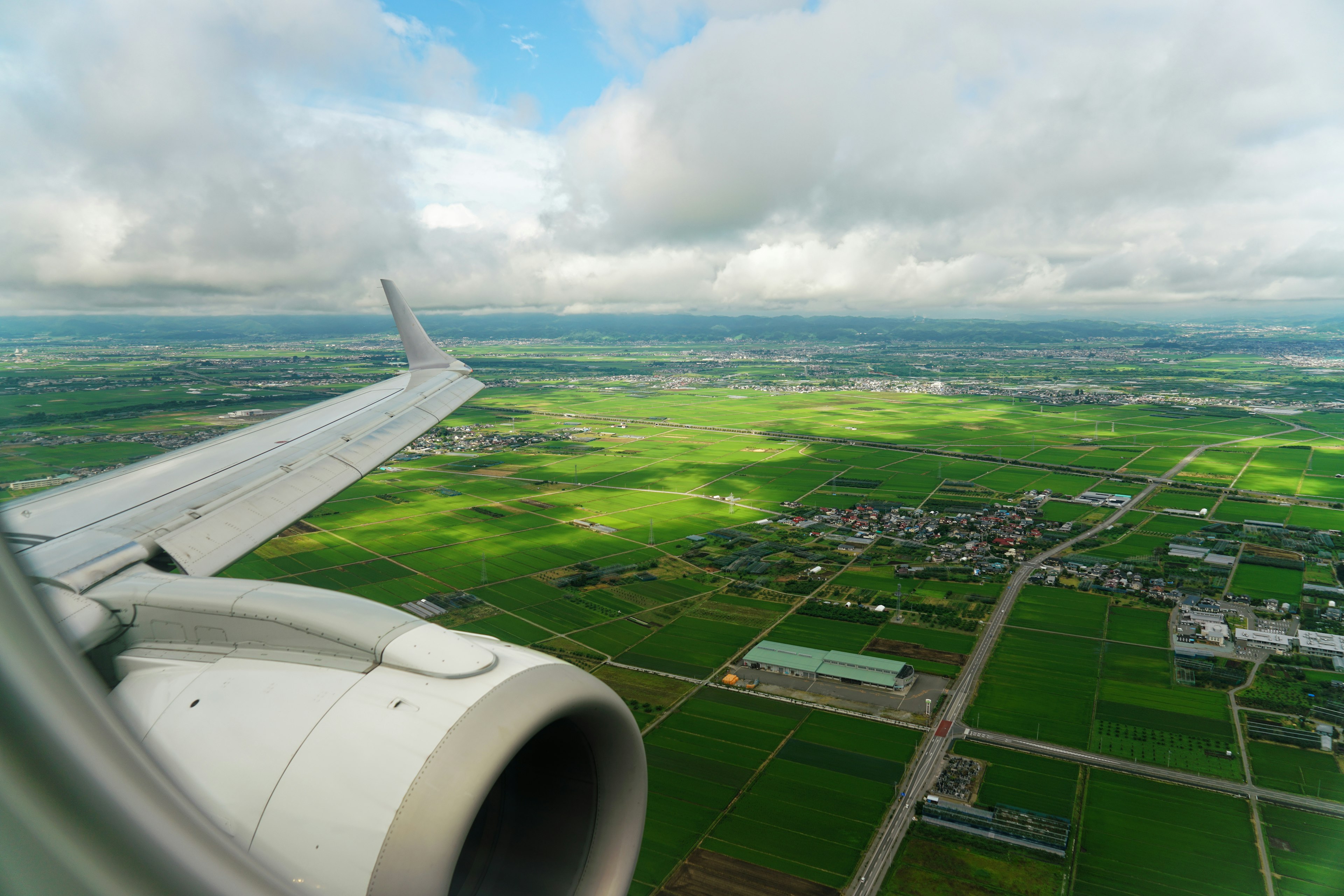 View from an airplane wing showcasing green fields and a rural landscape under a partly cloudy sky