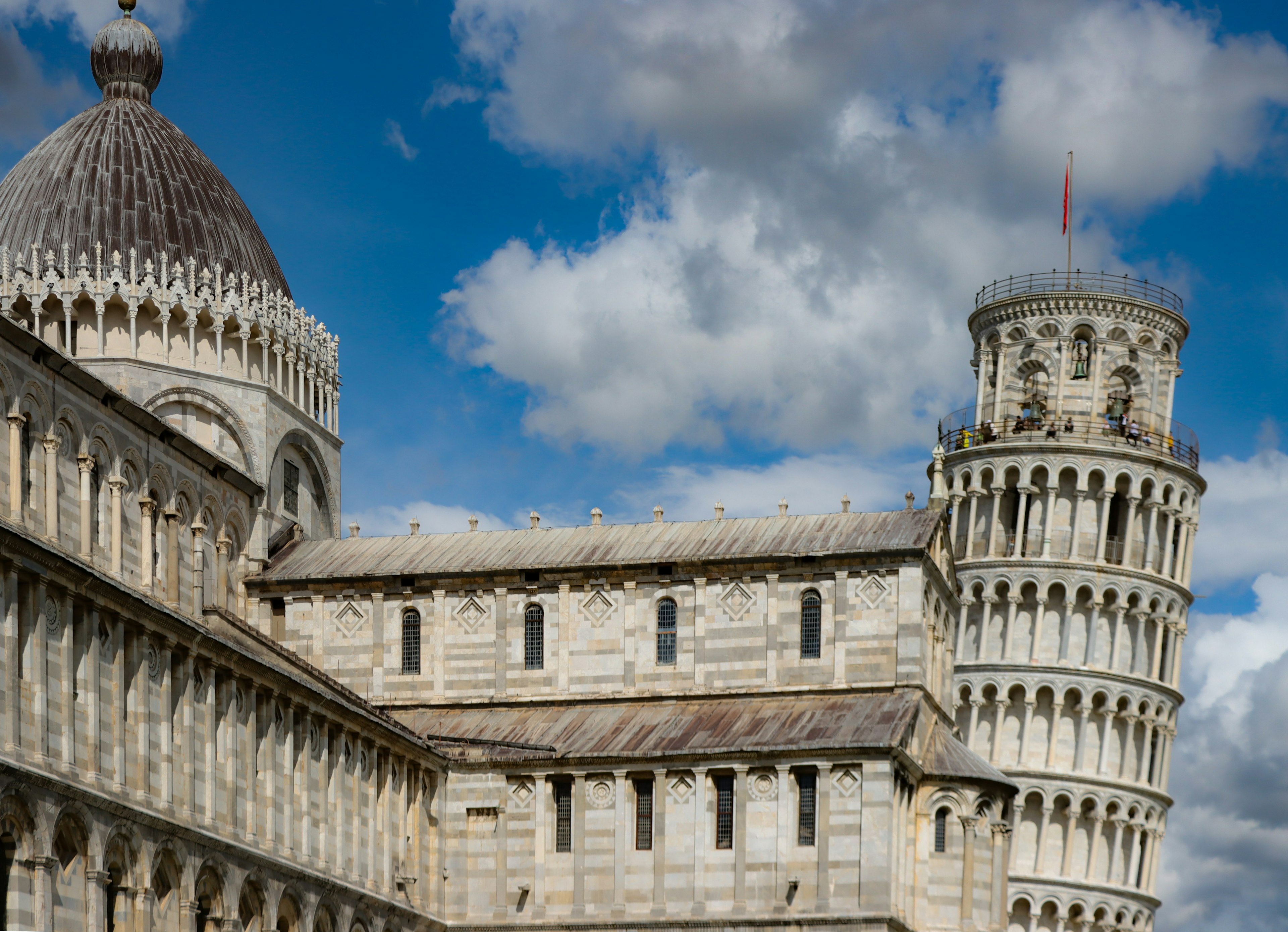 Bild des schiefen Turms von Pisa und der umliegenden Architektur mit weißen Wolken und blauem Himmel