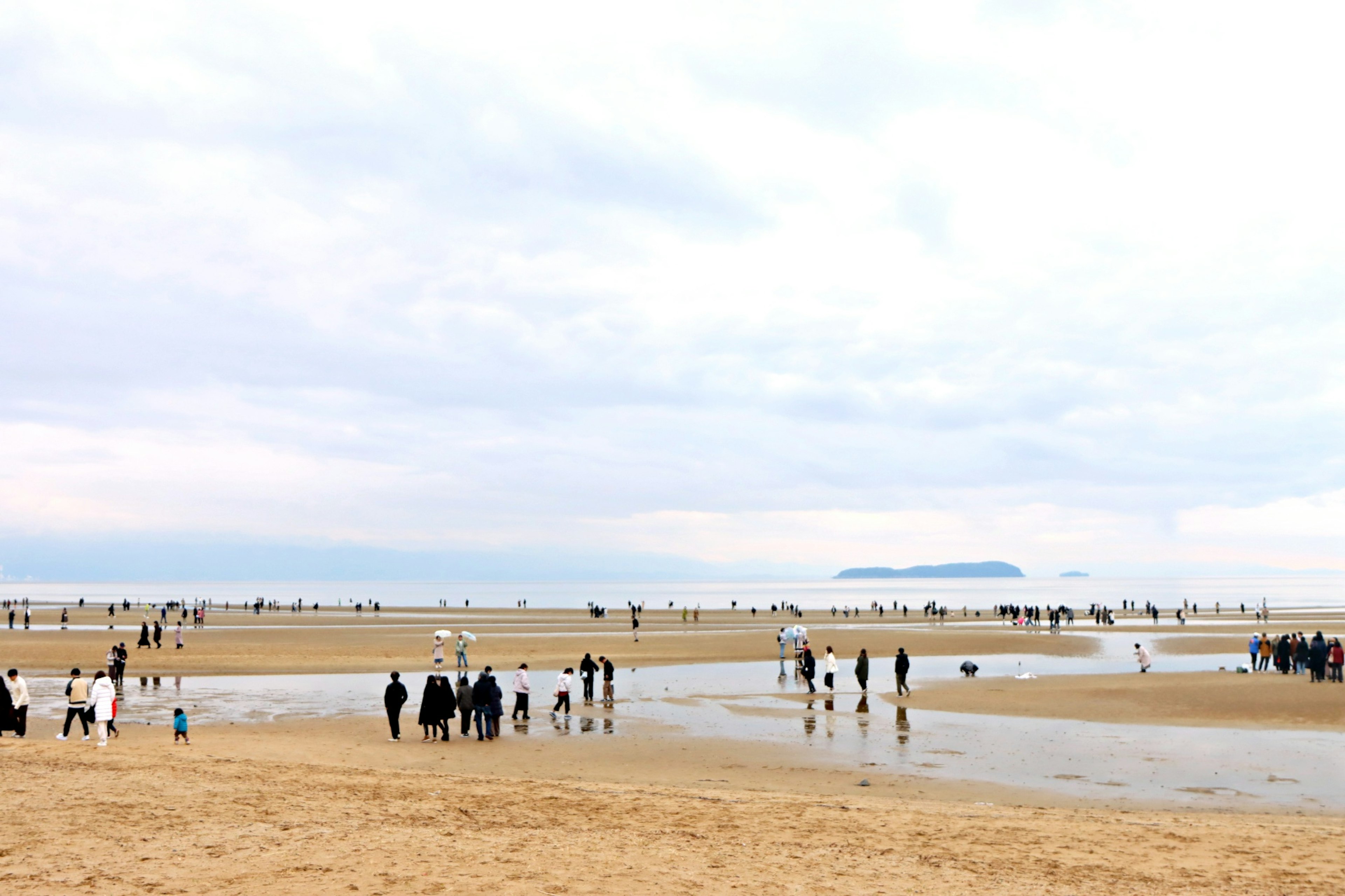 Menschenmenge an einem Strand mit nassem Sand und ruhiger See