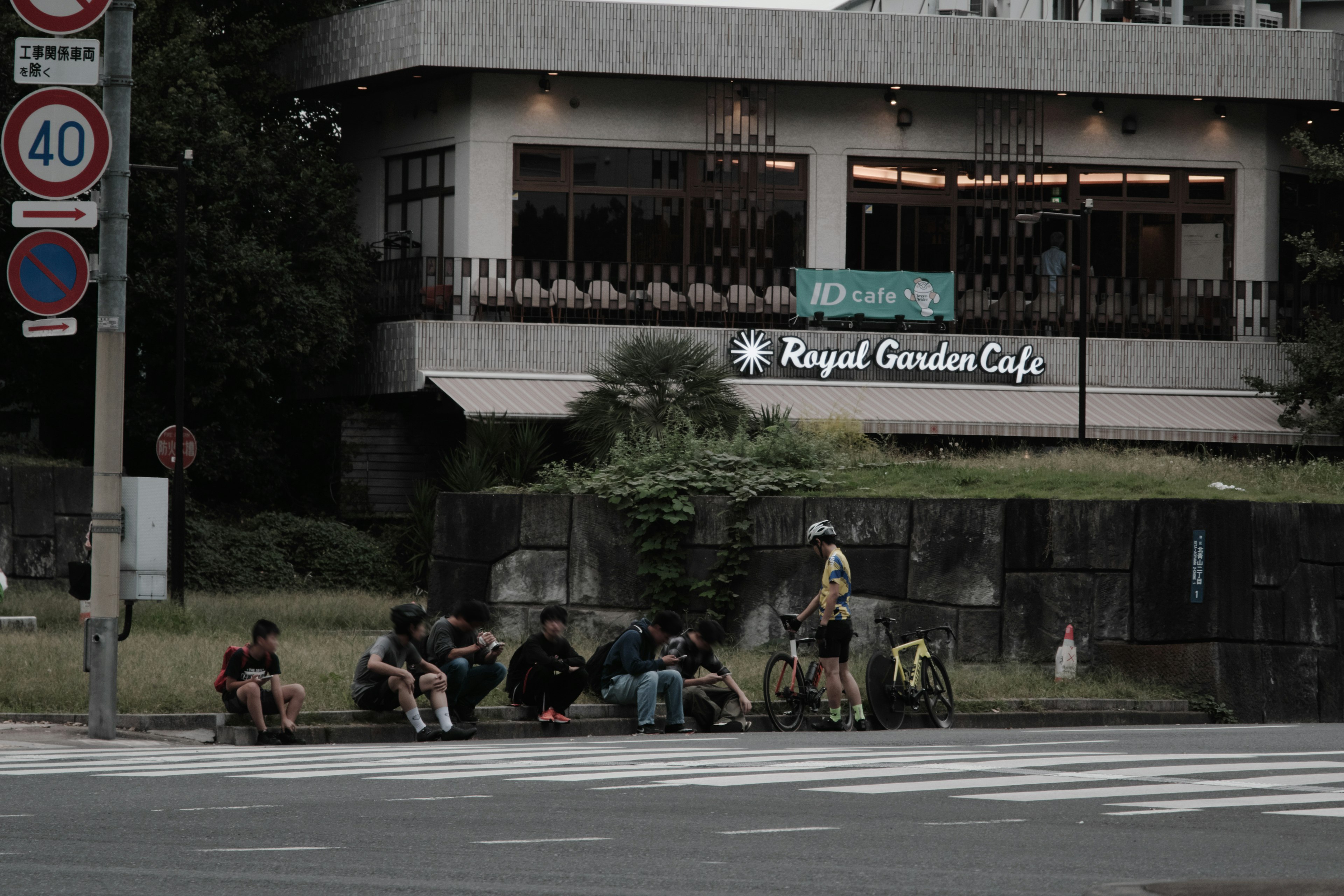 กลุ่มคนที่นั่งอยู่ที่มุมถนนพร้อมป้าย Royal Garden Cafe