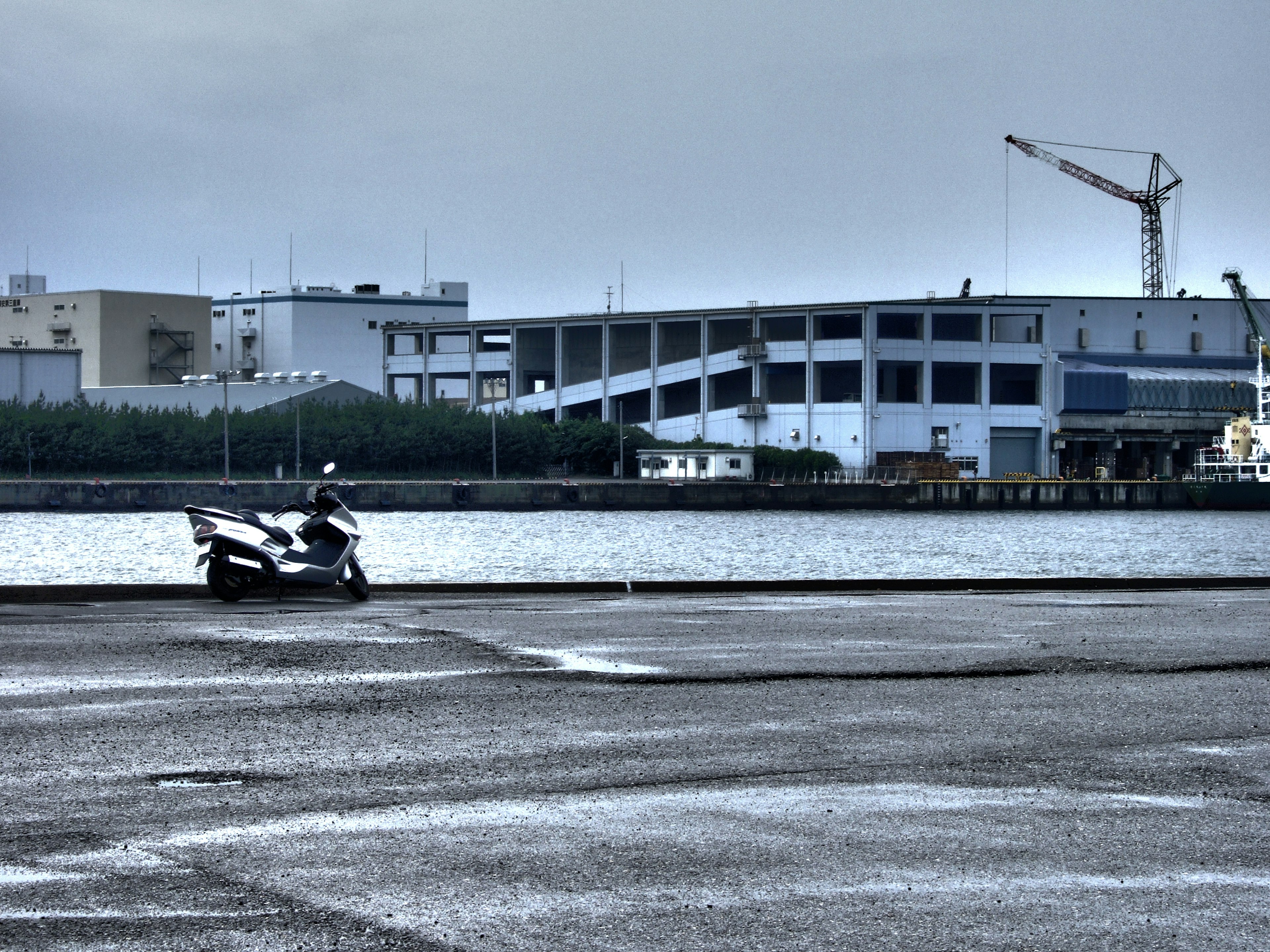 Scooter parked by the waterfront with industrial buildings in the background