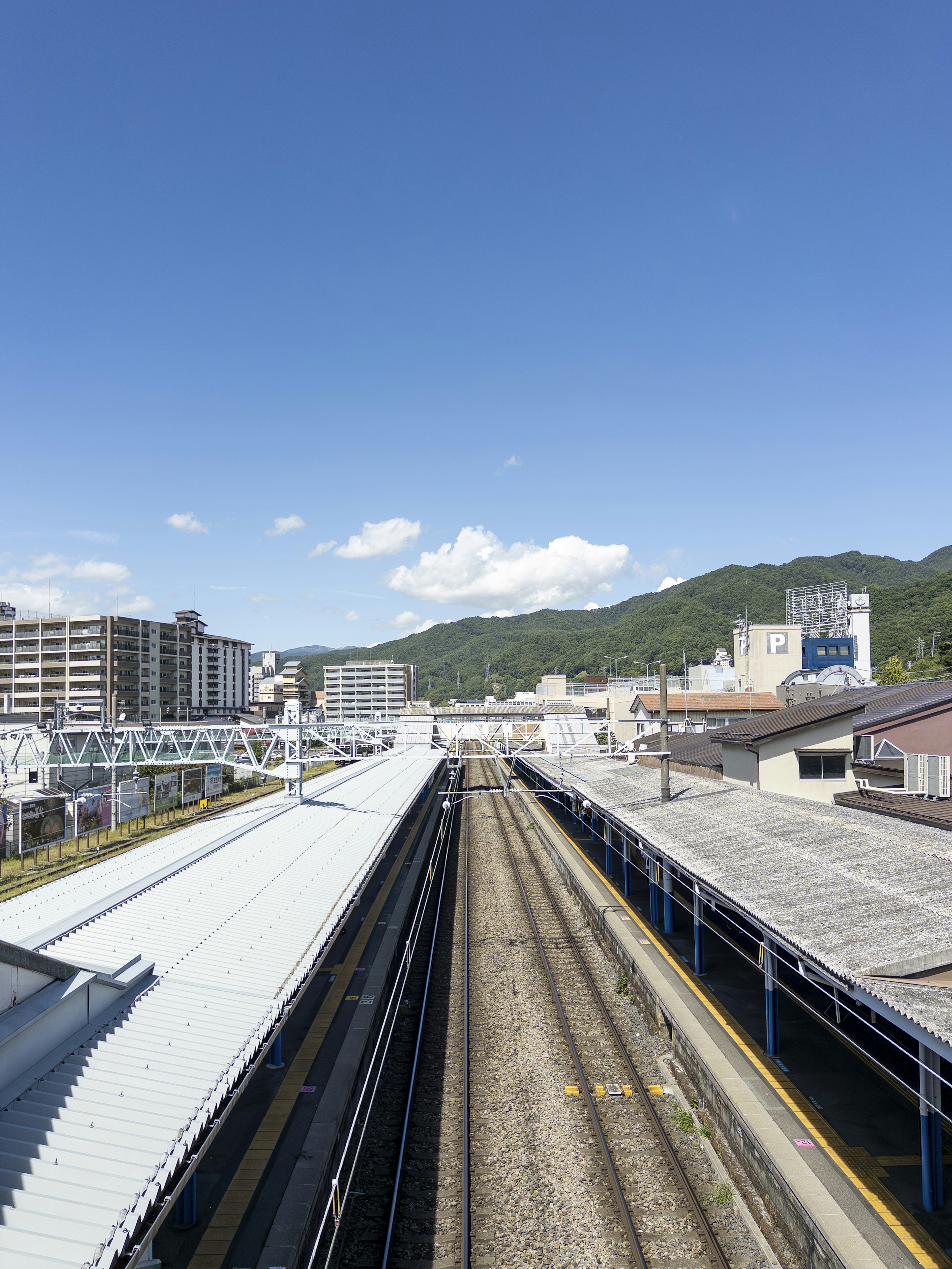 Pemandangan stasiun kereta di bawah langit biru dengan rel dan peron