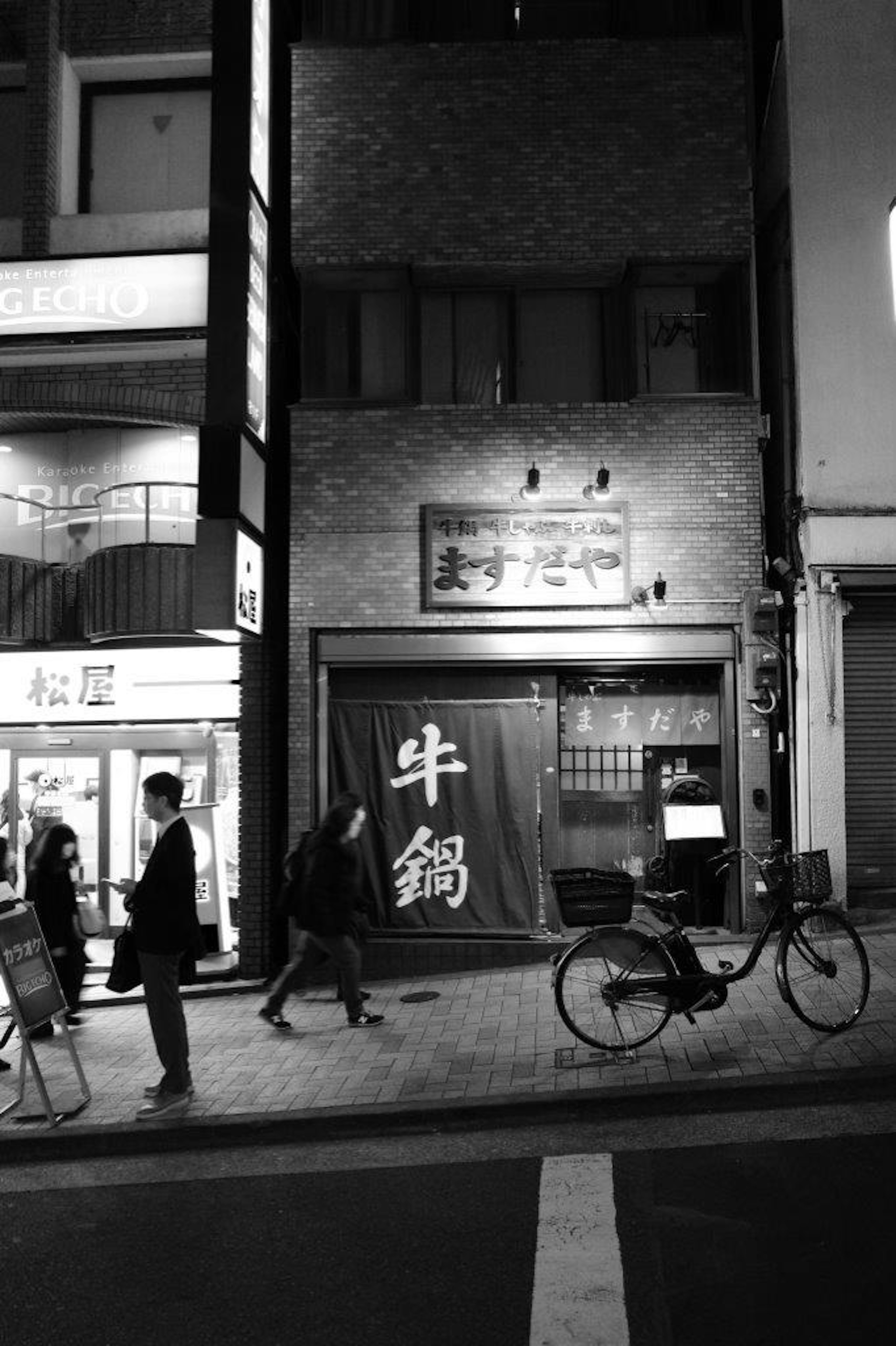 夜の東京の街並みにある牛鍋屋の店構えと通行人