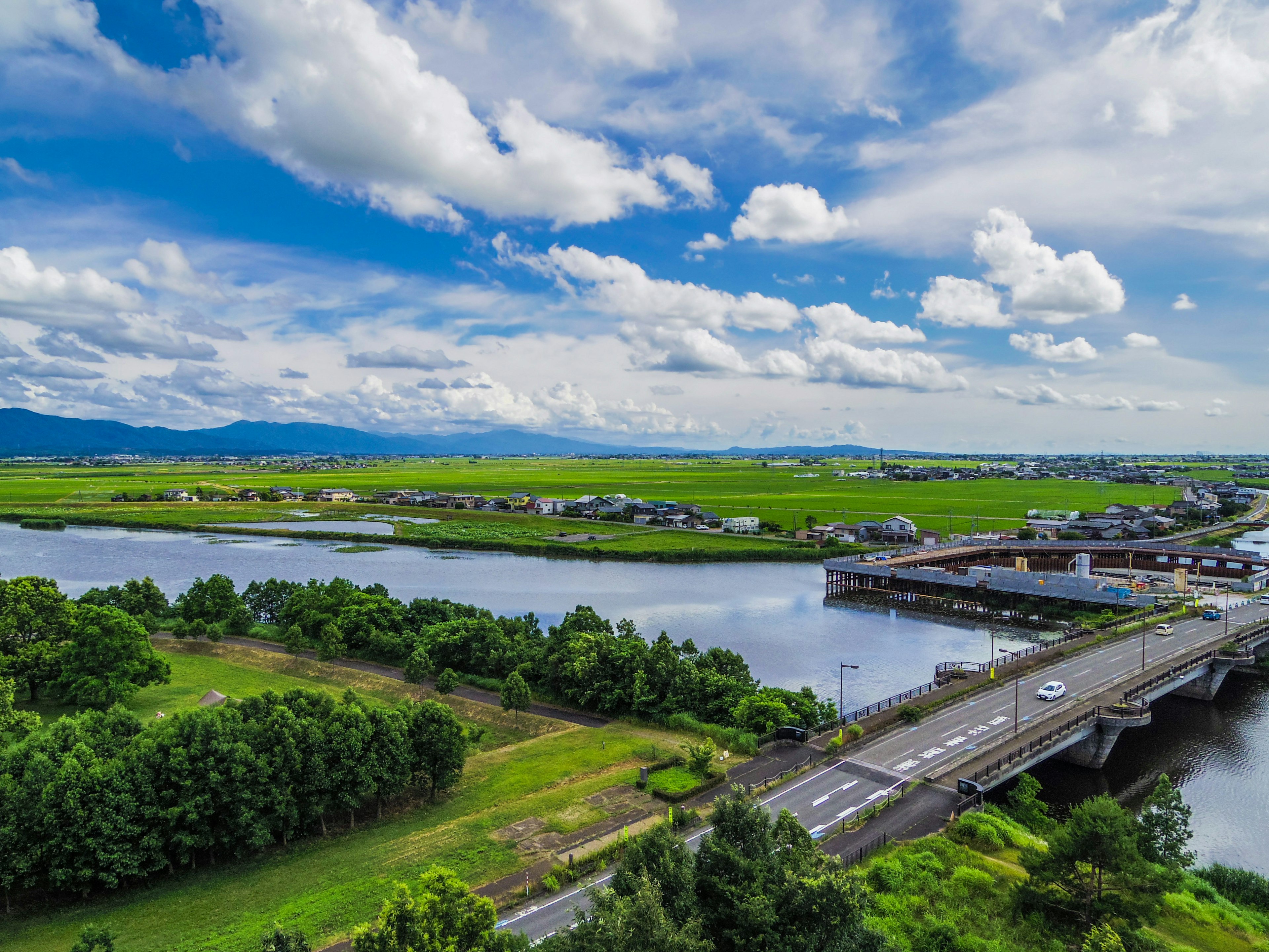 Paisaje verde con un río y un puente bajo un cielo azul y nubes blancas