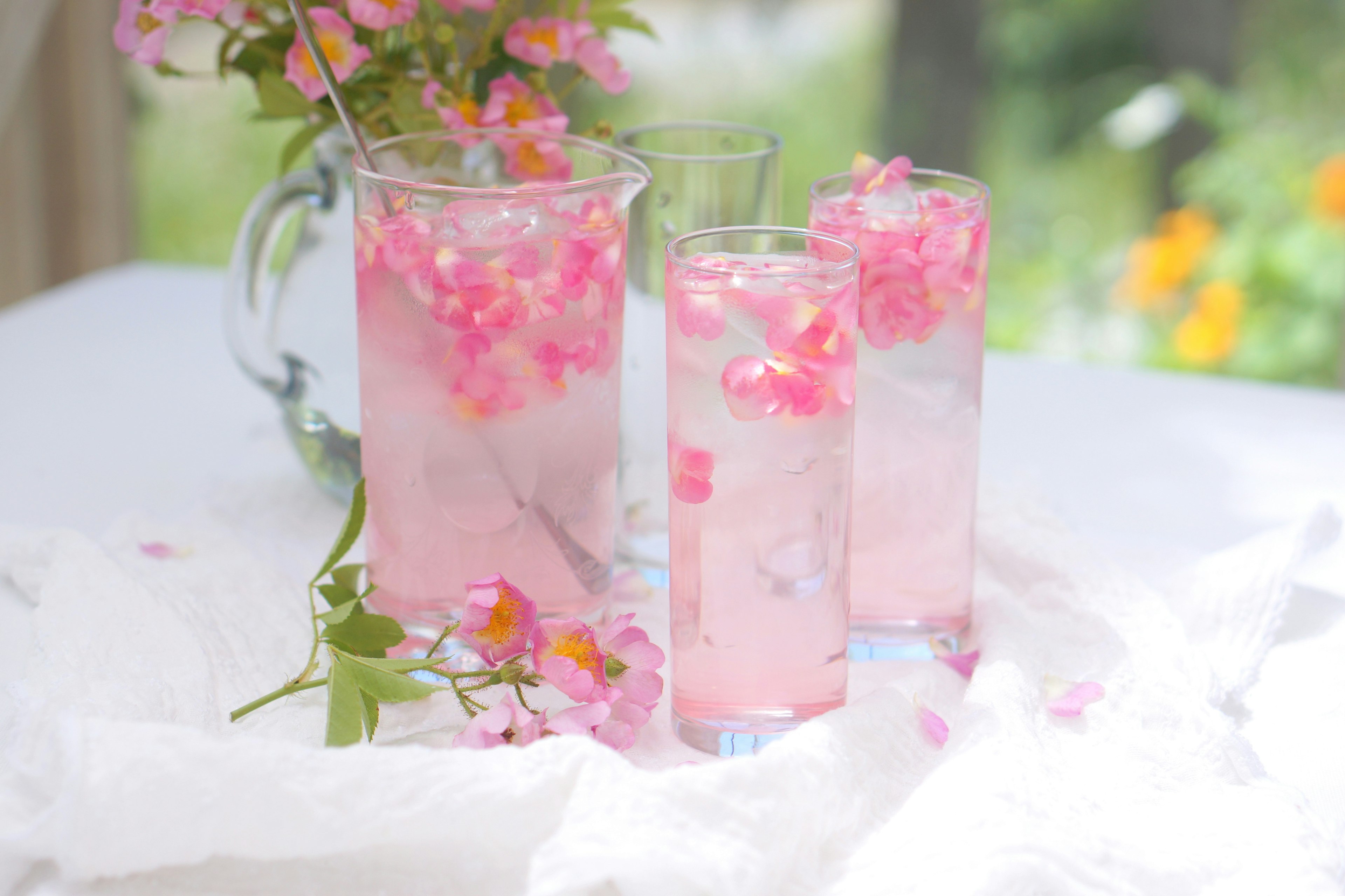 Tre bicchieri pieni di bevande infuse con fiori rosa su un tavolo con decorazioni floreali