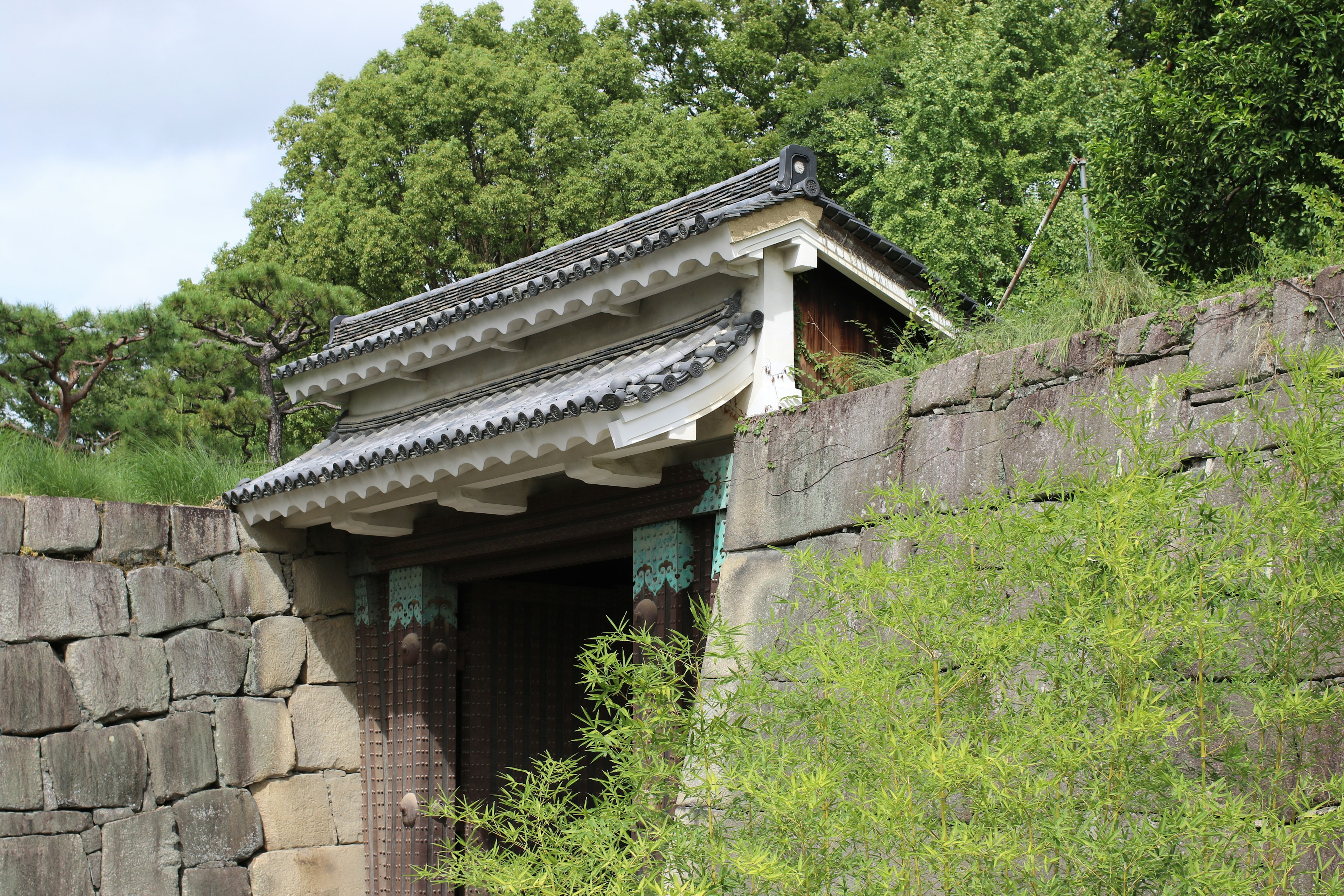 Puerta japonesa tradicional rodeada de vegetación y muro de piedra