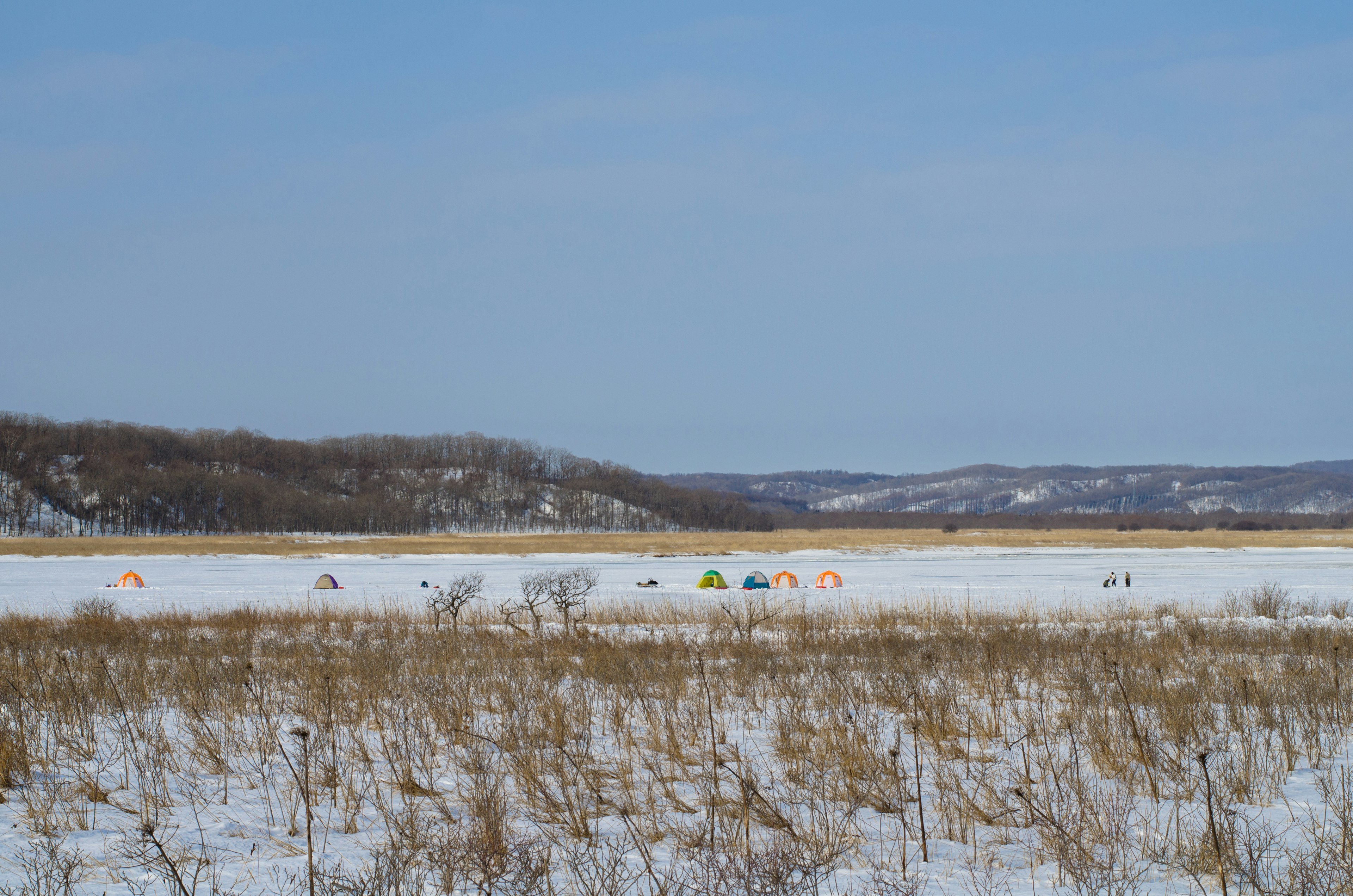 Group of camping tents on a snow-covered lake under a blue sky