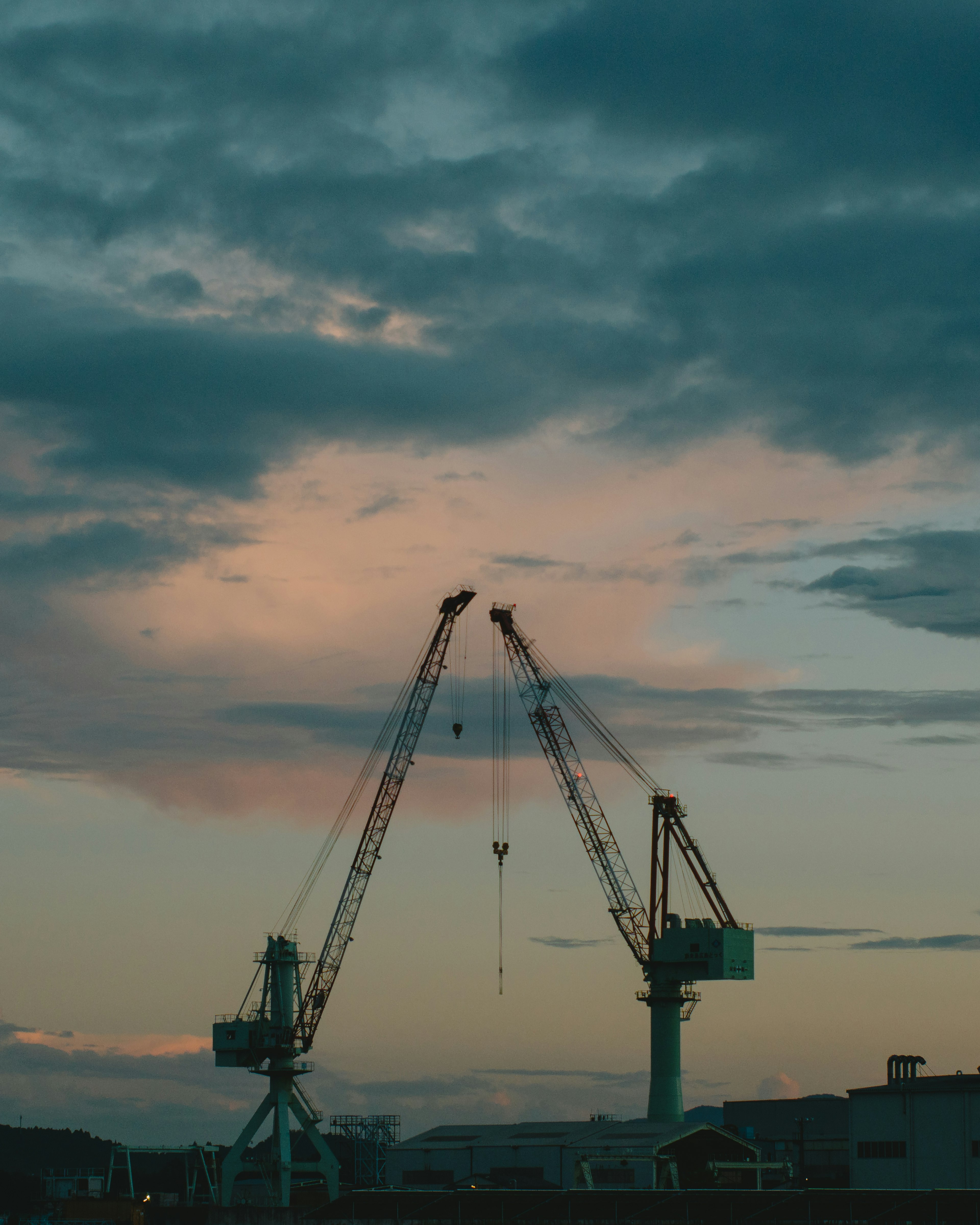 Silhouette von Kränen bei Dämmerung vor einem bewölkten Himmel