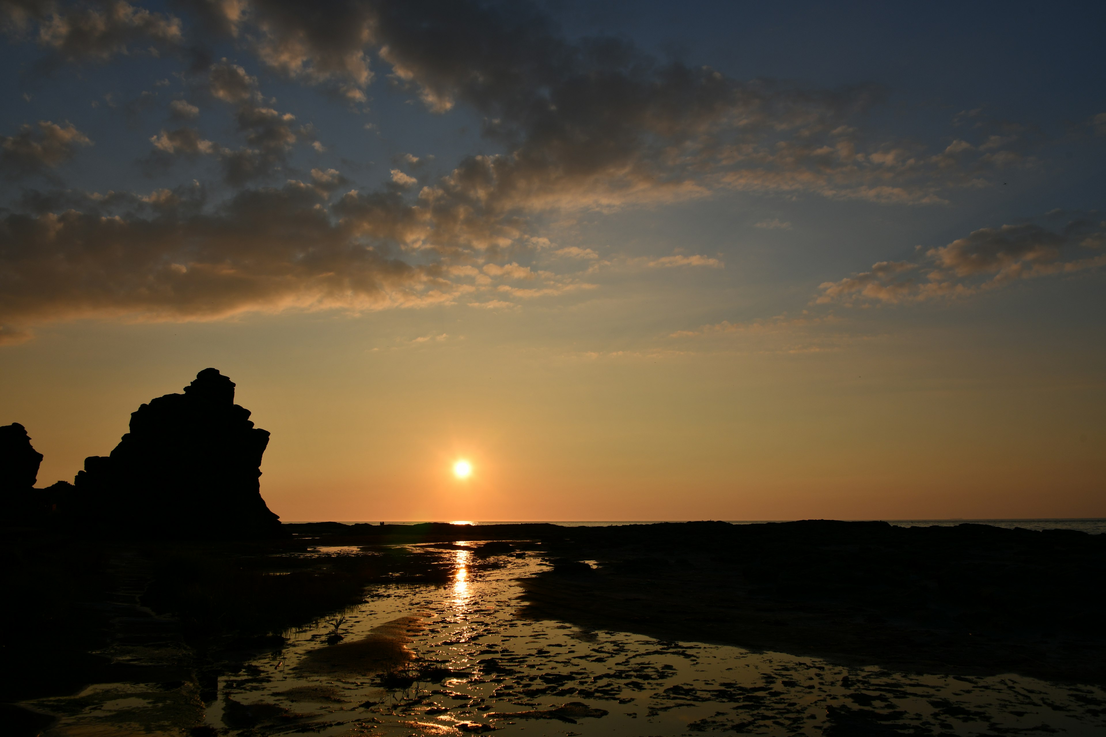 Escena de atardecer costero con rocas y reflejos en el agua