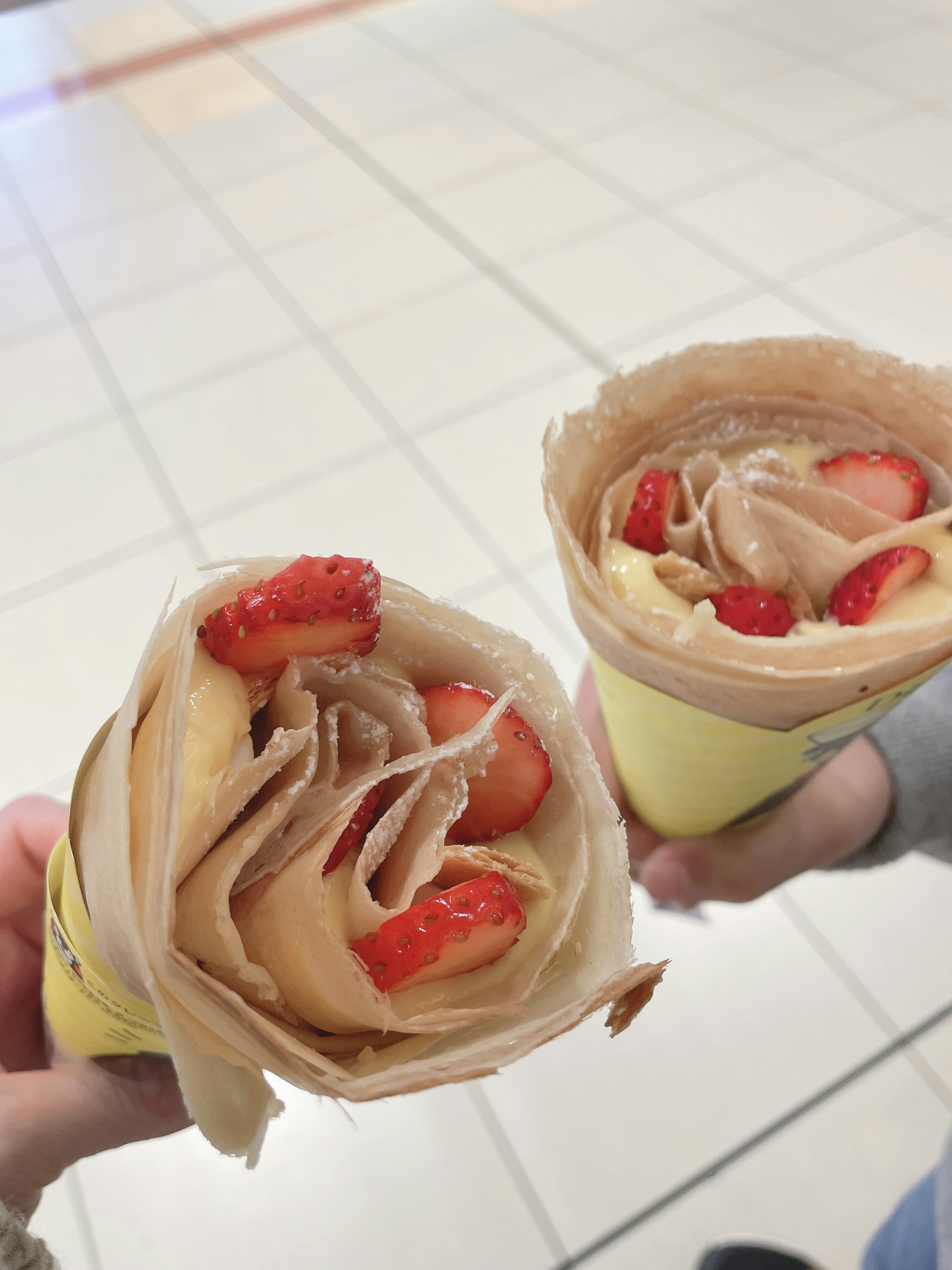 Two crepes held in hands with strawberries as toppings