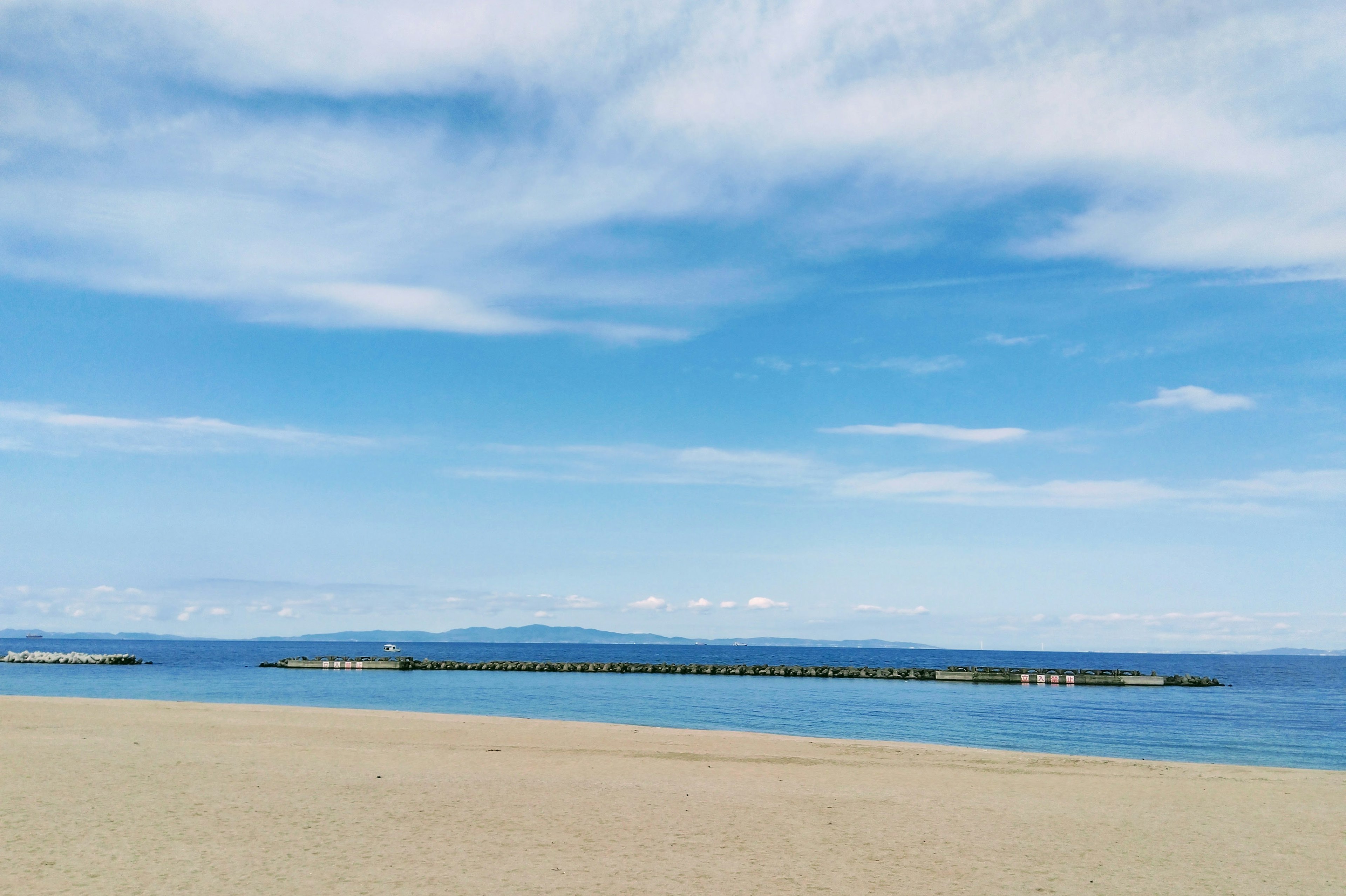 ทิวทัศน์ชายหาดมีท้องฟ้าสีฟ้าและทะเลมีชายหาดทรายและท่าเรือ