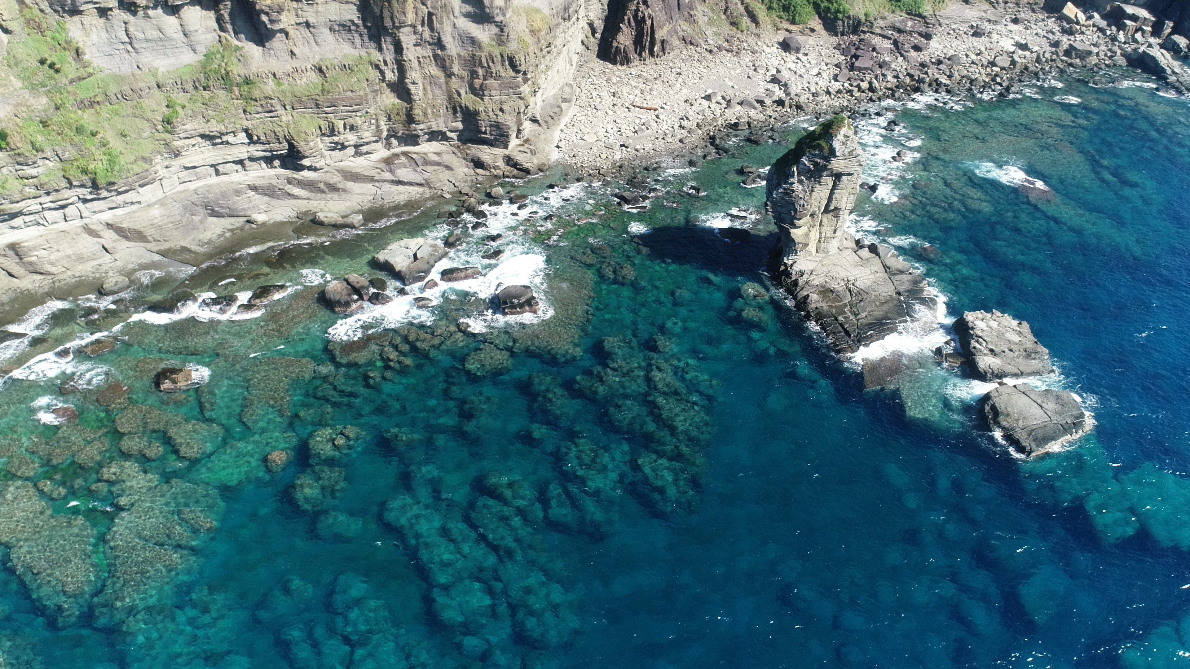 Vue aérienne d'une côte rocheuse avec une eau bleue claire et des rochers sous-marins visibles