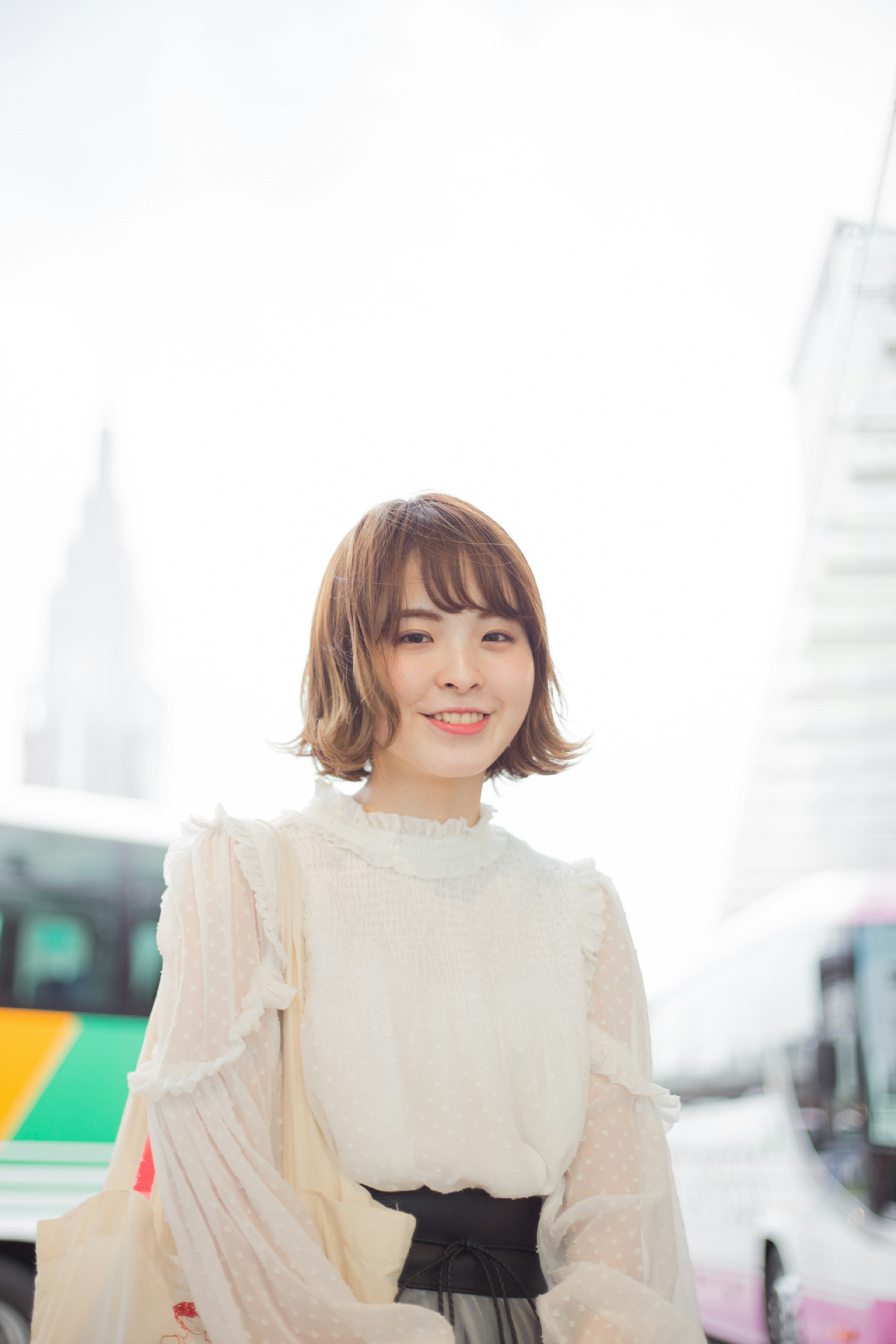 Portrait of a woman standing against a bright background smiling wearing a white blouse and black skirt