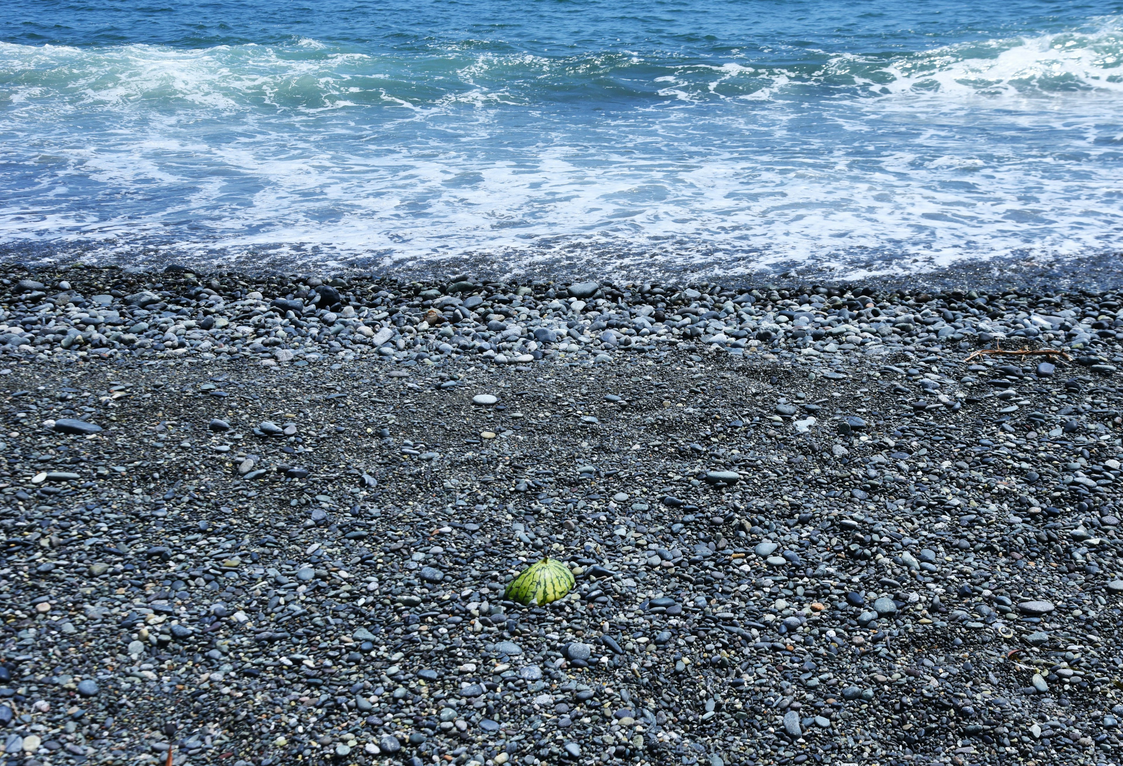 Green object on a pebbled beach with ocean waves