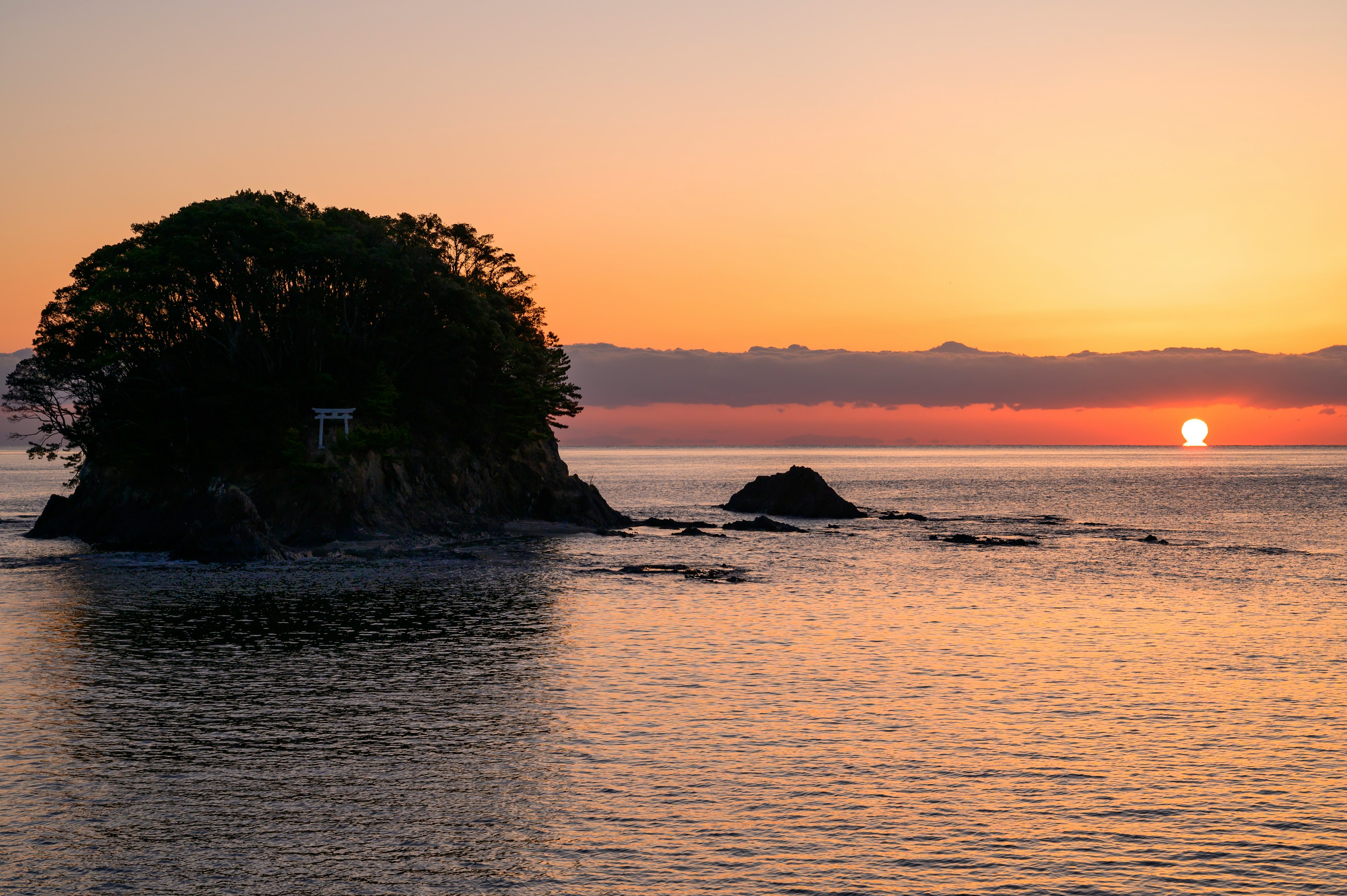 夕日が沈む海に浮かぶ小さな島と穏やかな波