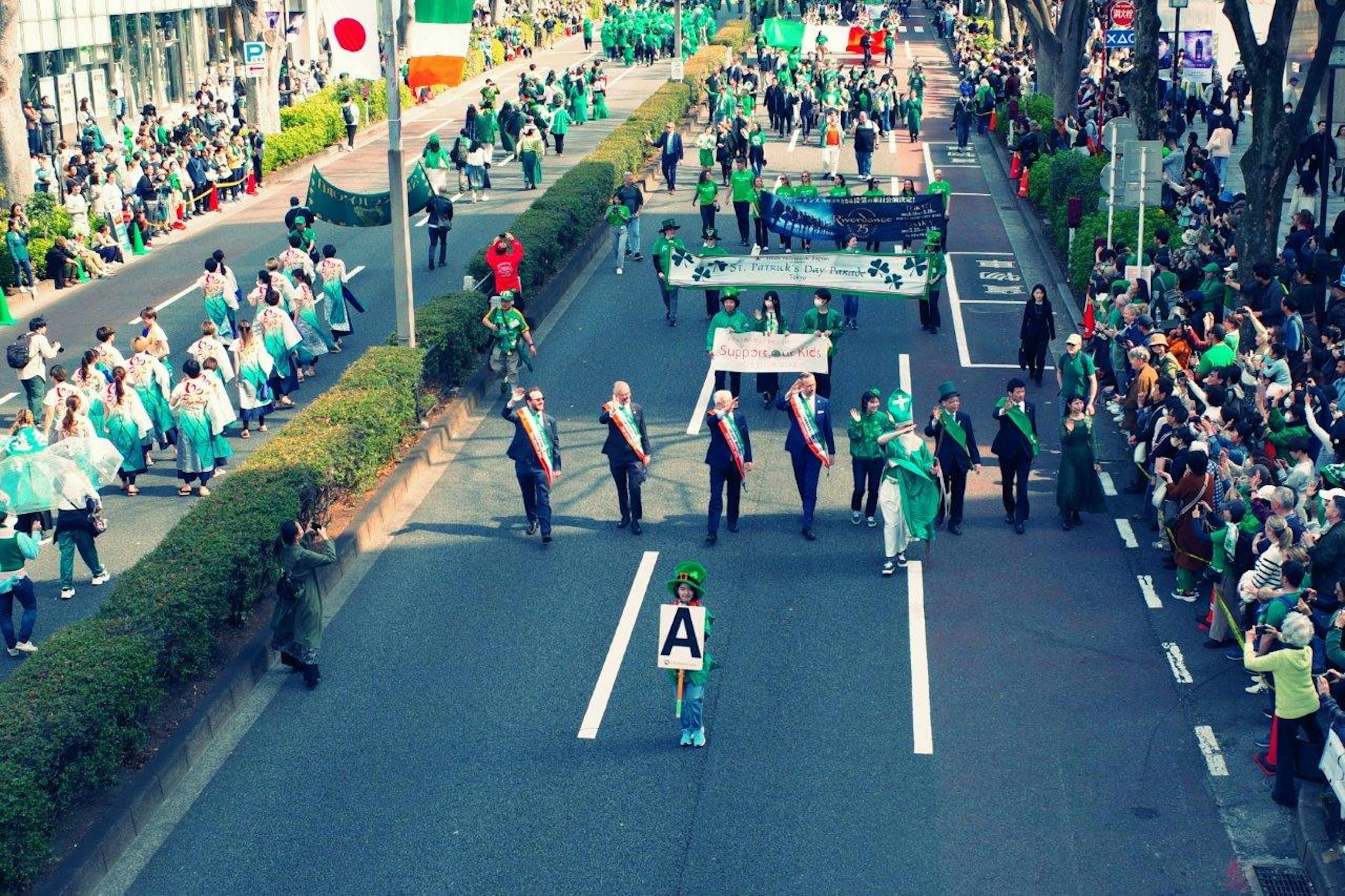 Una escena vibrante de desfile con participantes en trajes verdes y una multitud animando en una calle de la ciudad