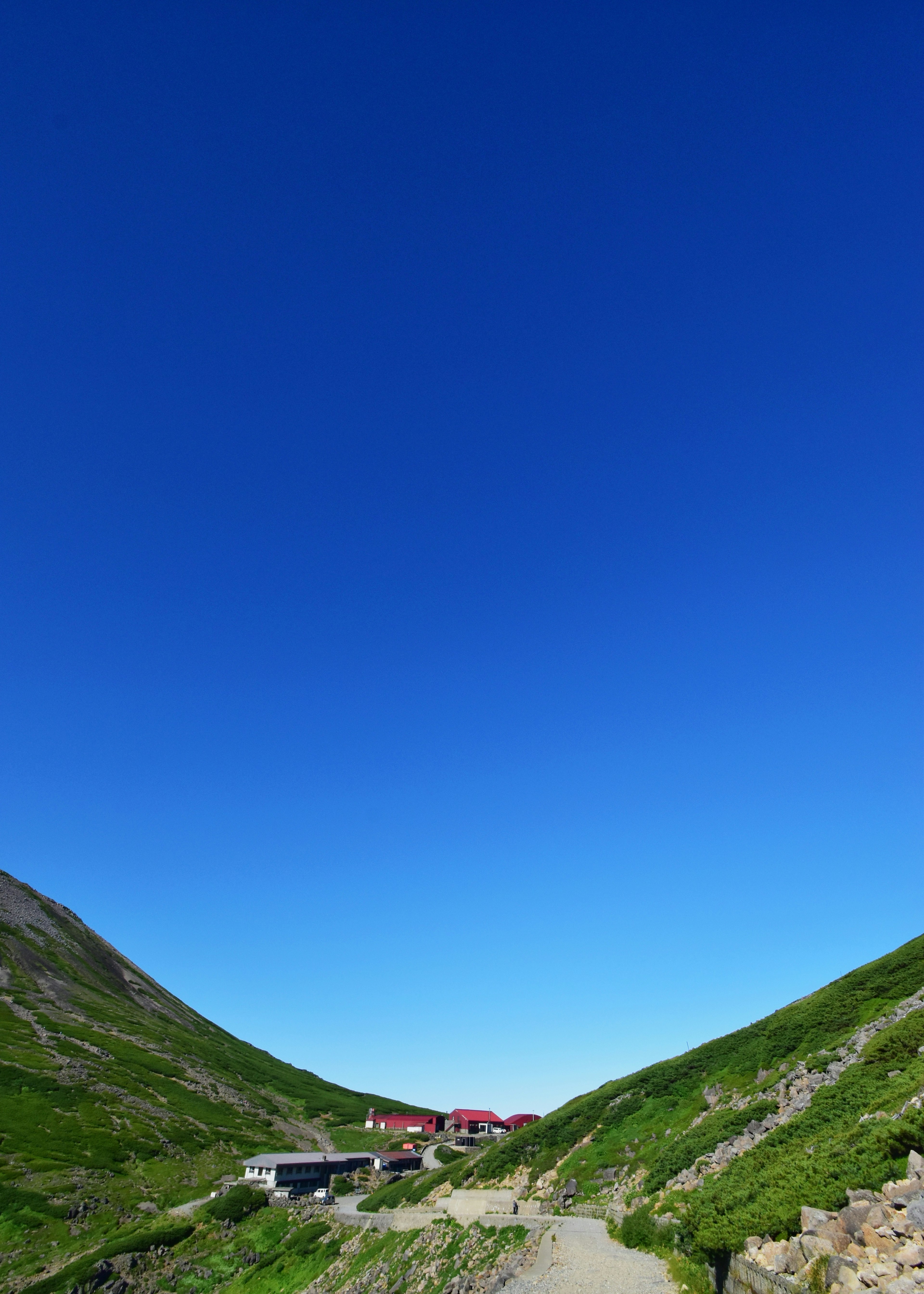 Pequeño edificio y camino situados entre montañas verdes bajo un cielo azul claro