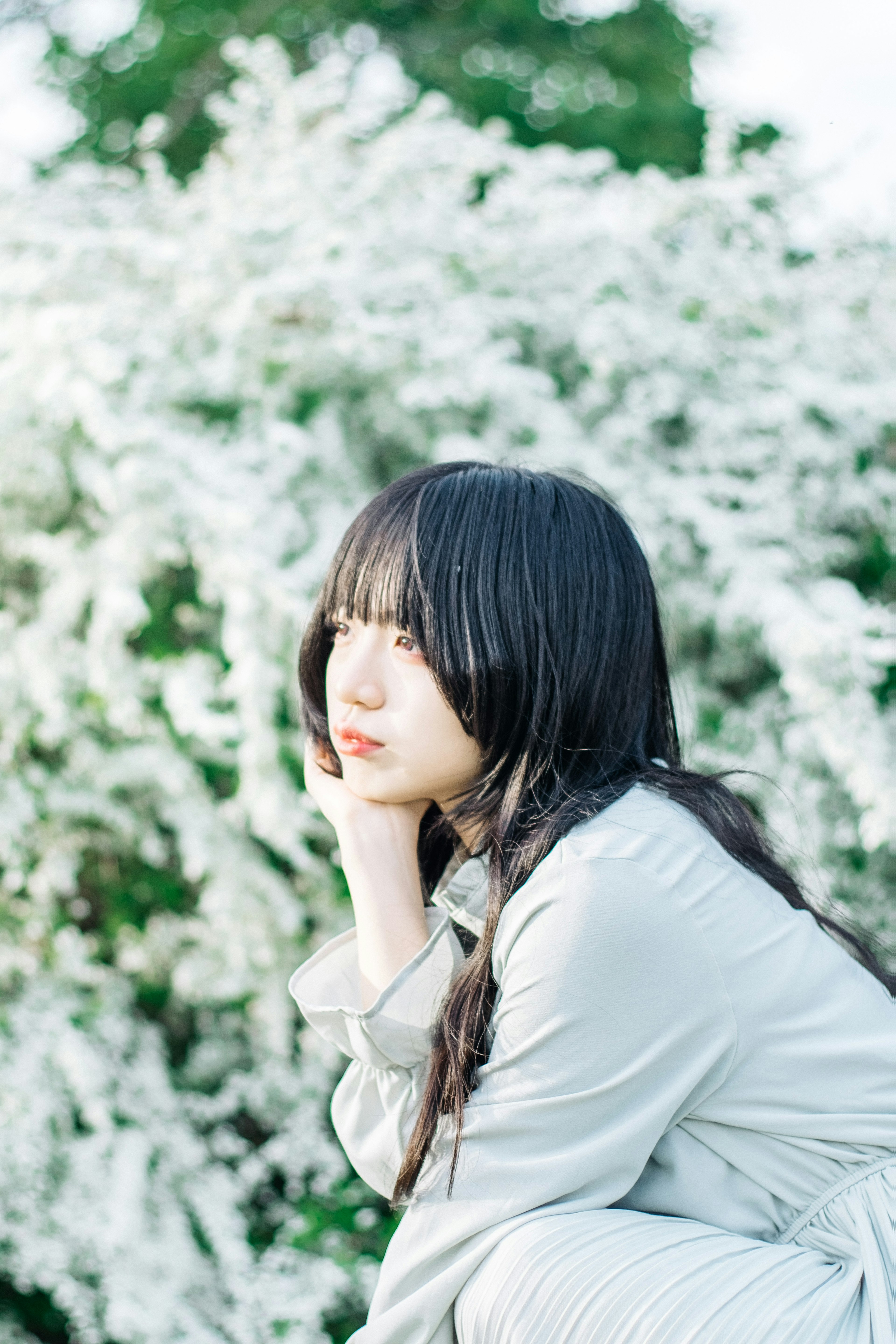 Side profile of a woman sitting in front of white flowers