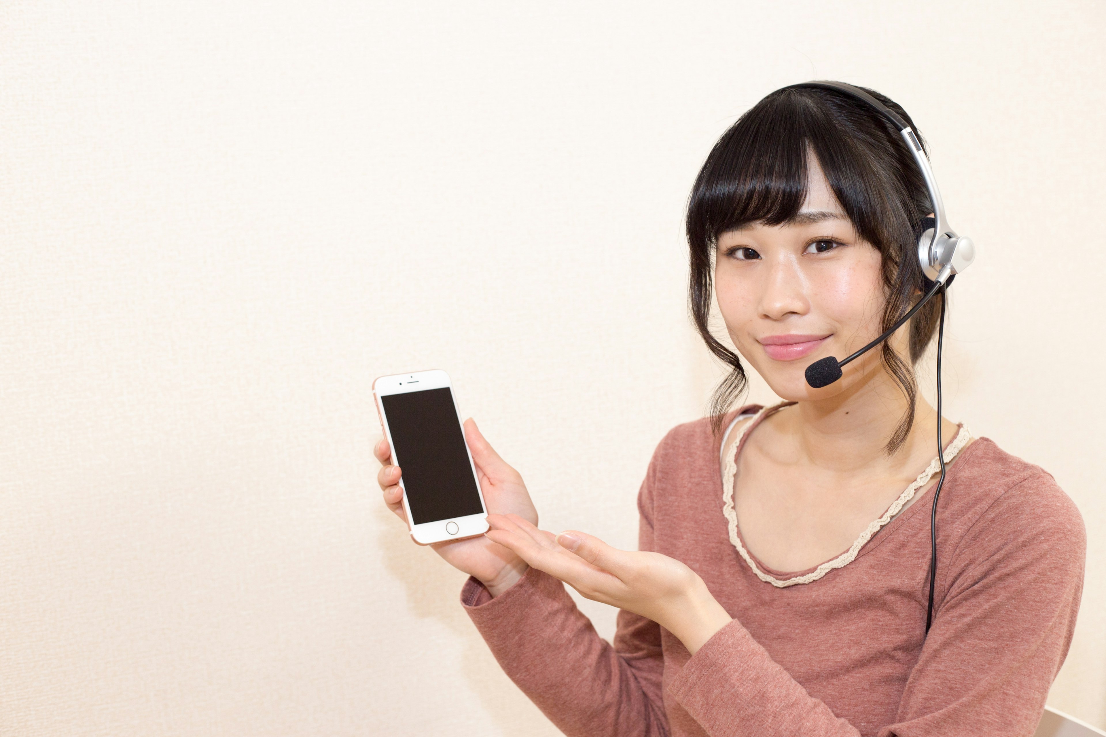 A woman wearing a headset smiling while holding a smartphone